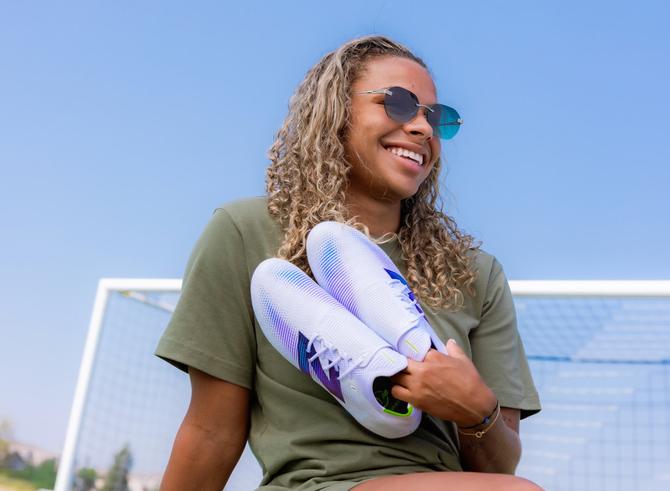Michelle Cooper smiling and holding a pair of soccer cleats