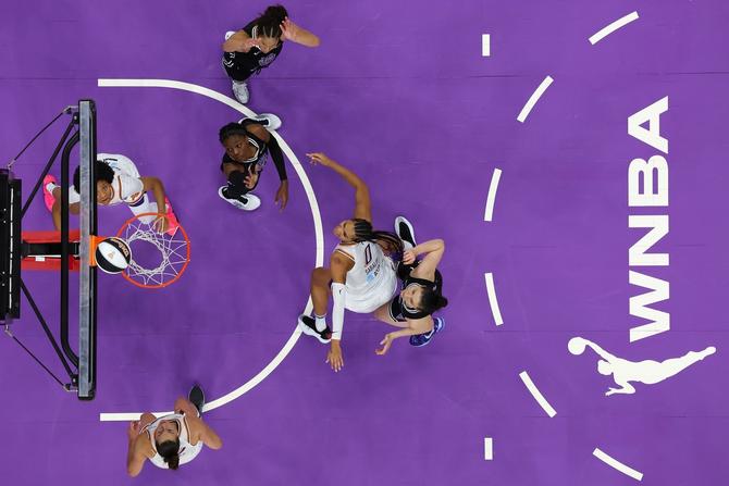 An overhead shot of a purple court with Phoenix Mercury and Golden State Valkyries players battling for a rebound.
