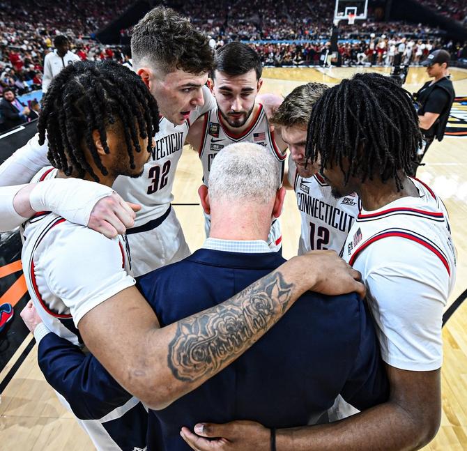 The No. 1–seed UConn men’s basketball team huddles during their Final Four win over No. 4 Alabama on Saturday.