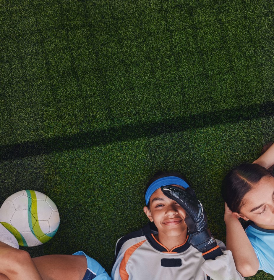 Girls lying on a soccer field looking up at the camera smiling