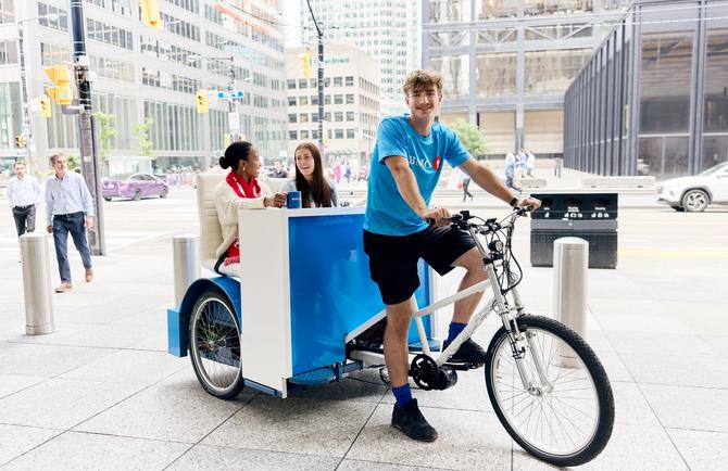 Two people riding a BMO sponsored rickshaw in downtown Toronto