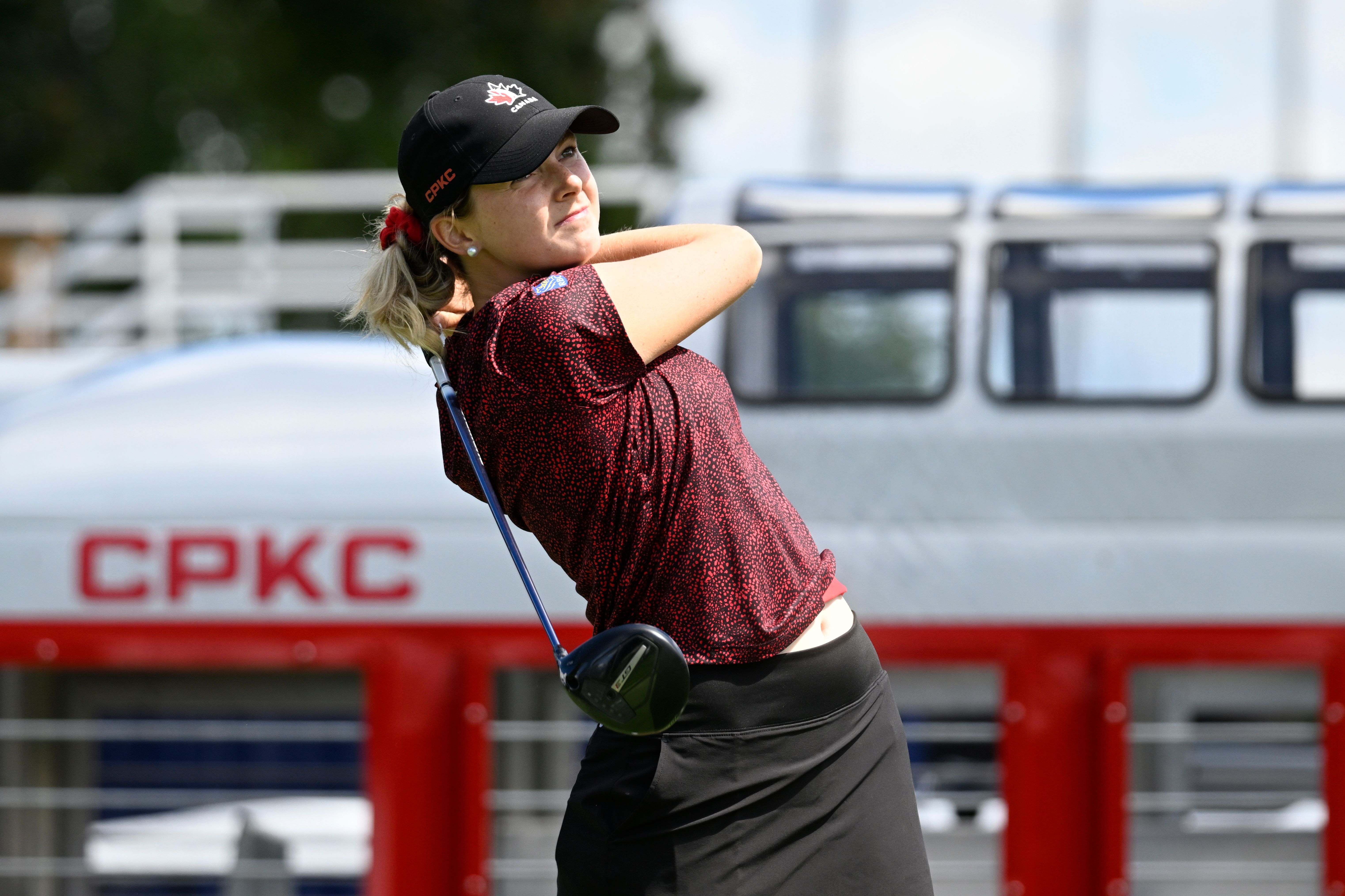 Golfer in a black cap and red shirt finishing a swing at the CPKC Women’s Open.