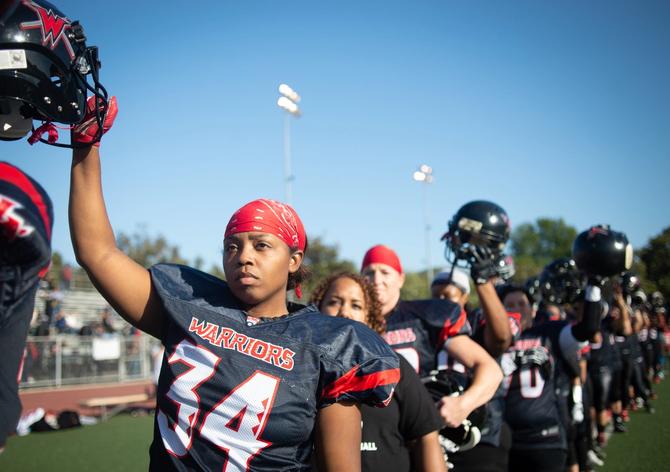 LA Warriors women's tackle football team raise their helmets for the national anthem before their game against the Portland Fighting Shockwave at Rancho Cienega Stadium on June 30, 2018 in Los Angeles, California. The Warriors won the game 39-6 and will advance to the next round of playoffs to be held in Kansas City on July 14.