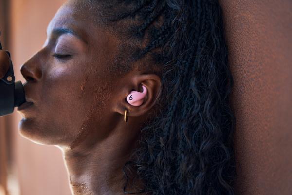 A woman wearing Powerbeats Fit while drinking water
