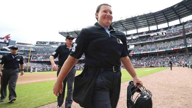Jen Pawol smiling while holding her umpire’s mask on the field