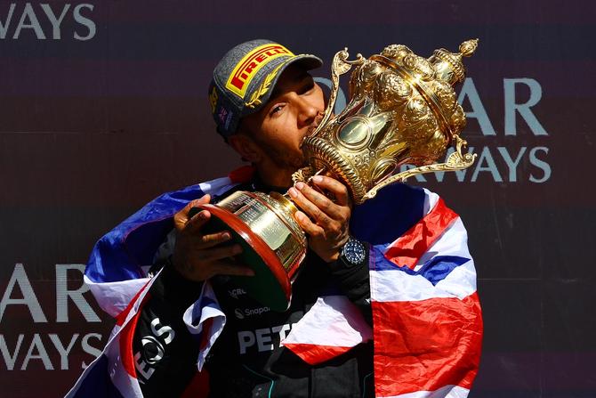 Race winner Lewis Hamilton of Mercedes stands on the podium, covered by the Union Jack, as he kisses his first-place trophy.
