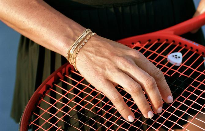 A person's hand on a tennis racket with bracelets on their wrist