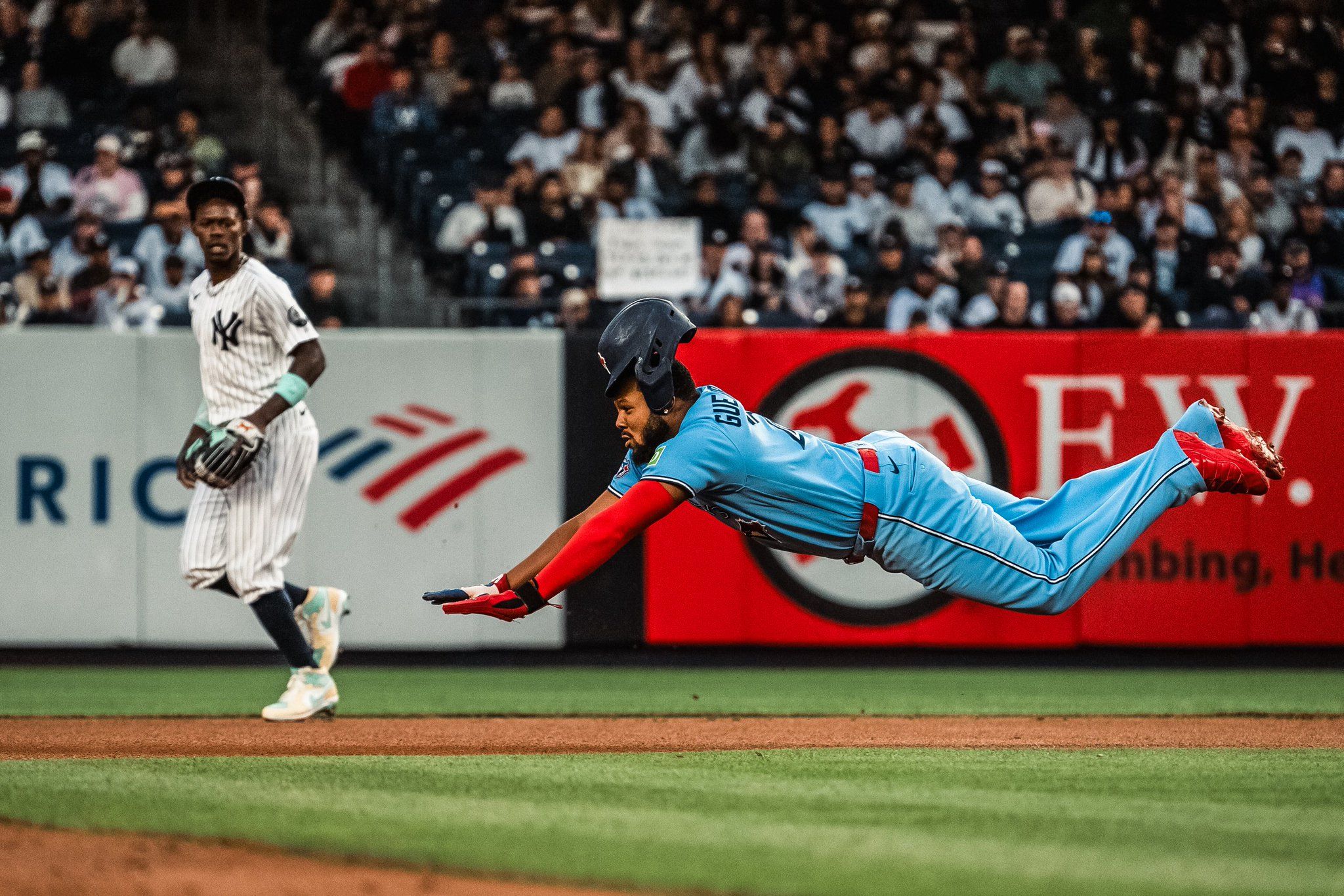 Vladimir Guerrero Jr. of the Toronto Blue Jays dives toward a base while a Yankees player looks on. 