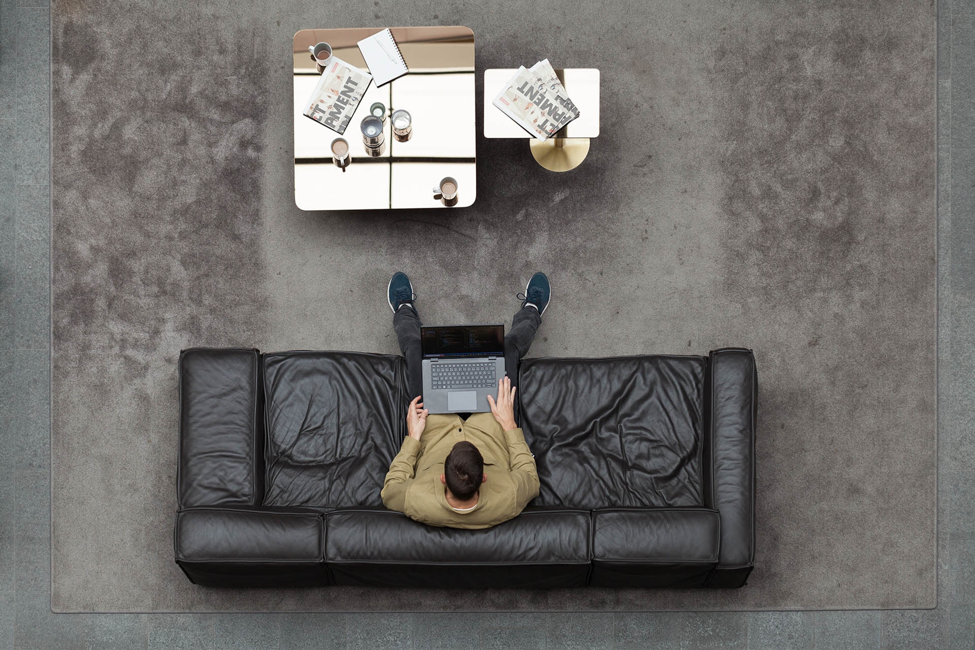 A man working on a laptop computer in a leather sofa photographed from above