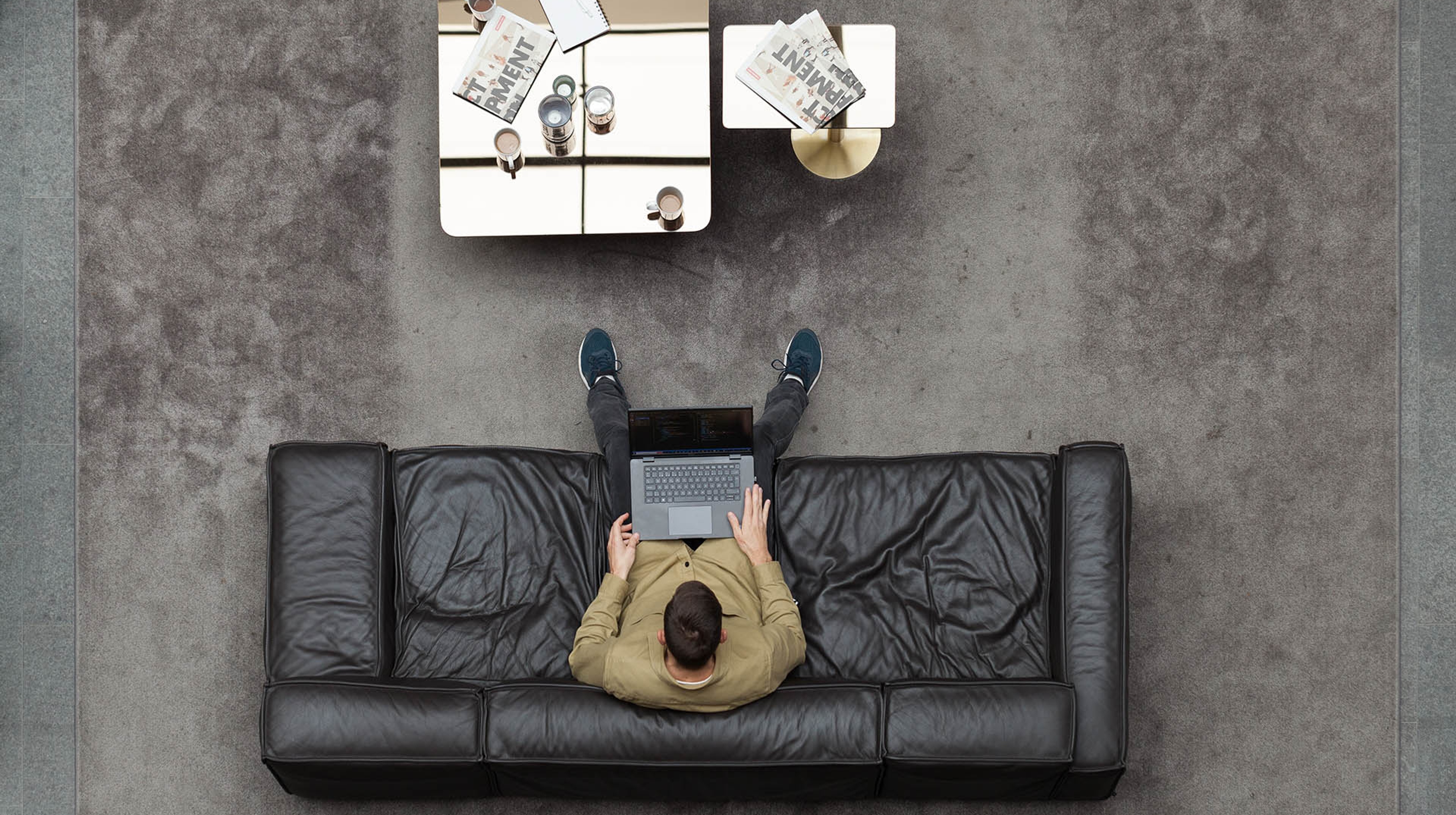 A man working on a laptop computer in a leather sofa photographed from above