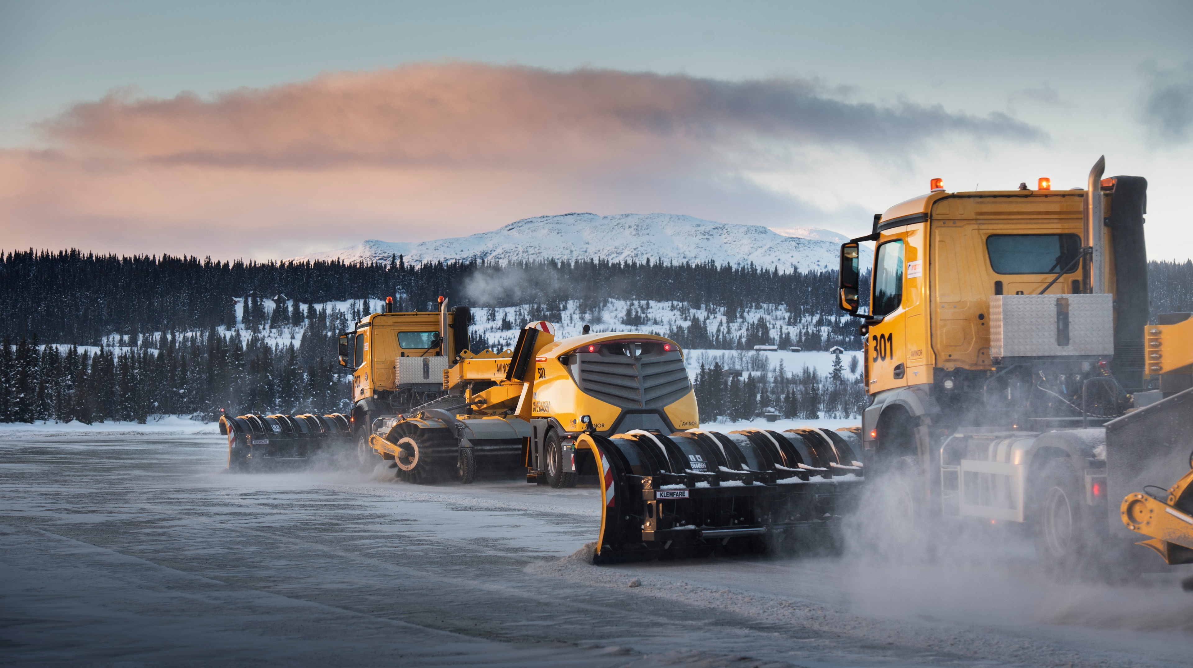 Two snowlpoughs at airport with snowy mountains in the background