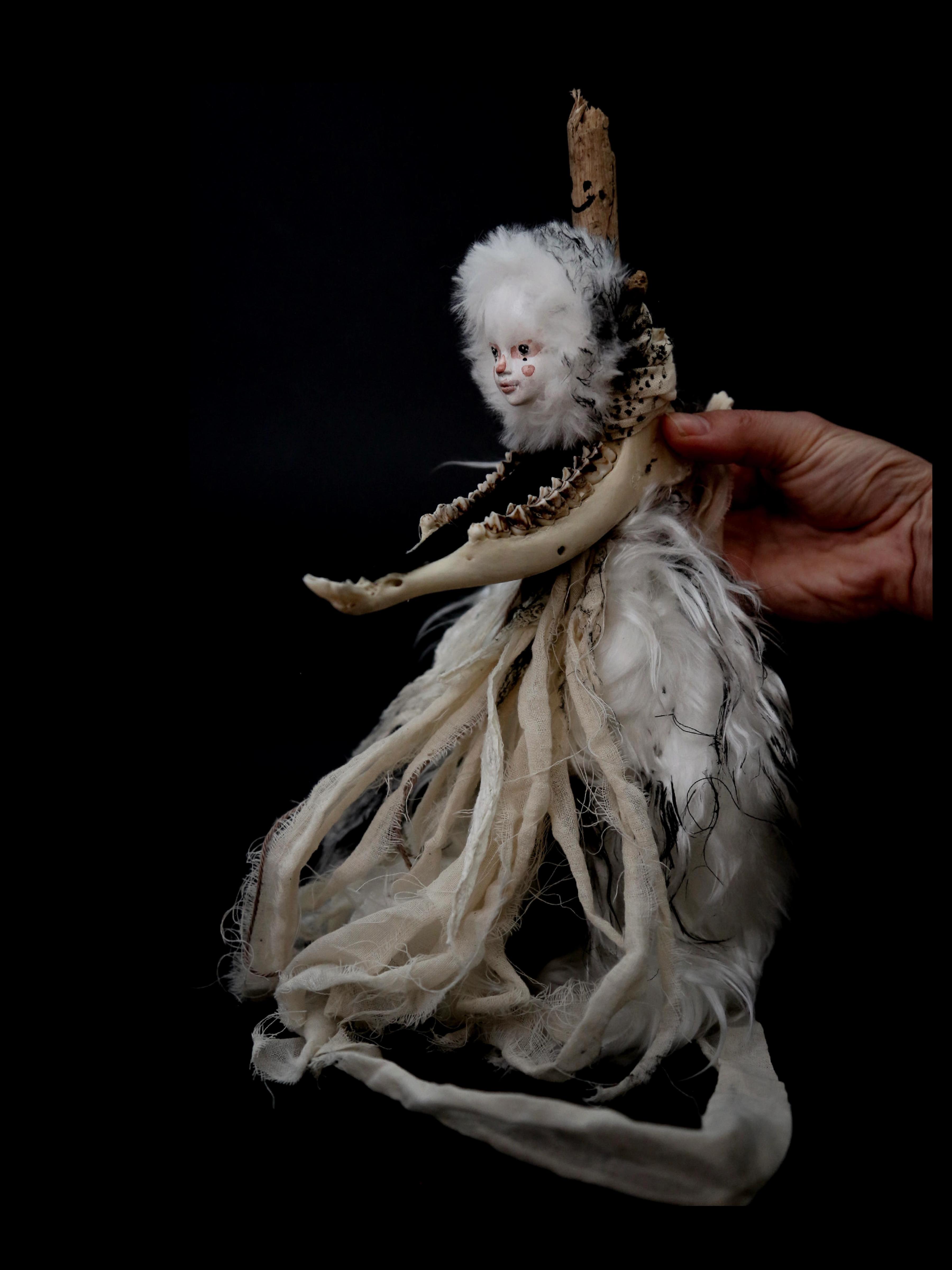 A puppet made out of plus, fabric, bones and a white puppet face, held by the artis claudia Six