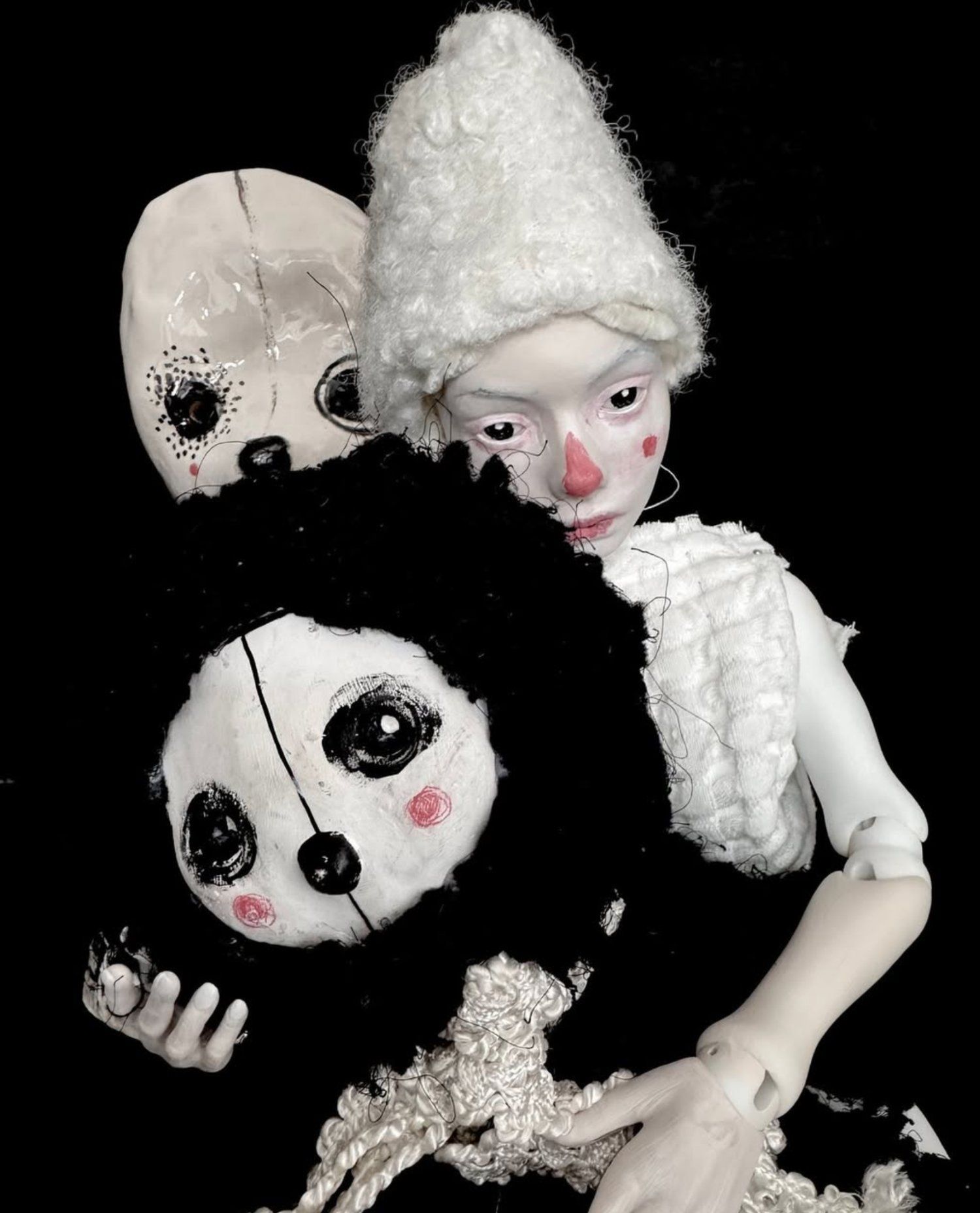 Ball-jointed doll holding two soft sculpture creatures — a tender trio in black and white, gazing outward