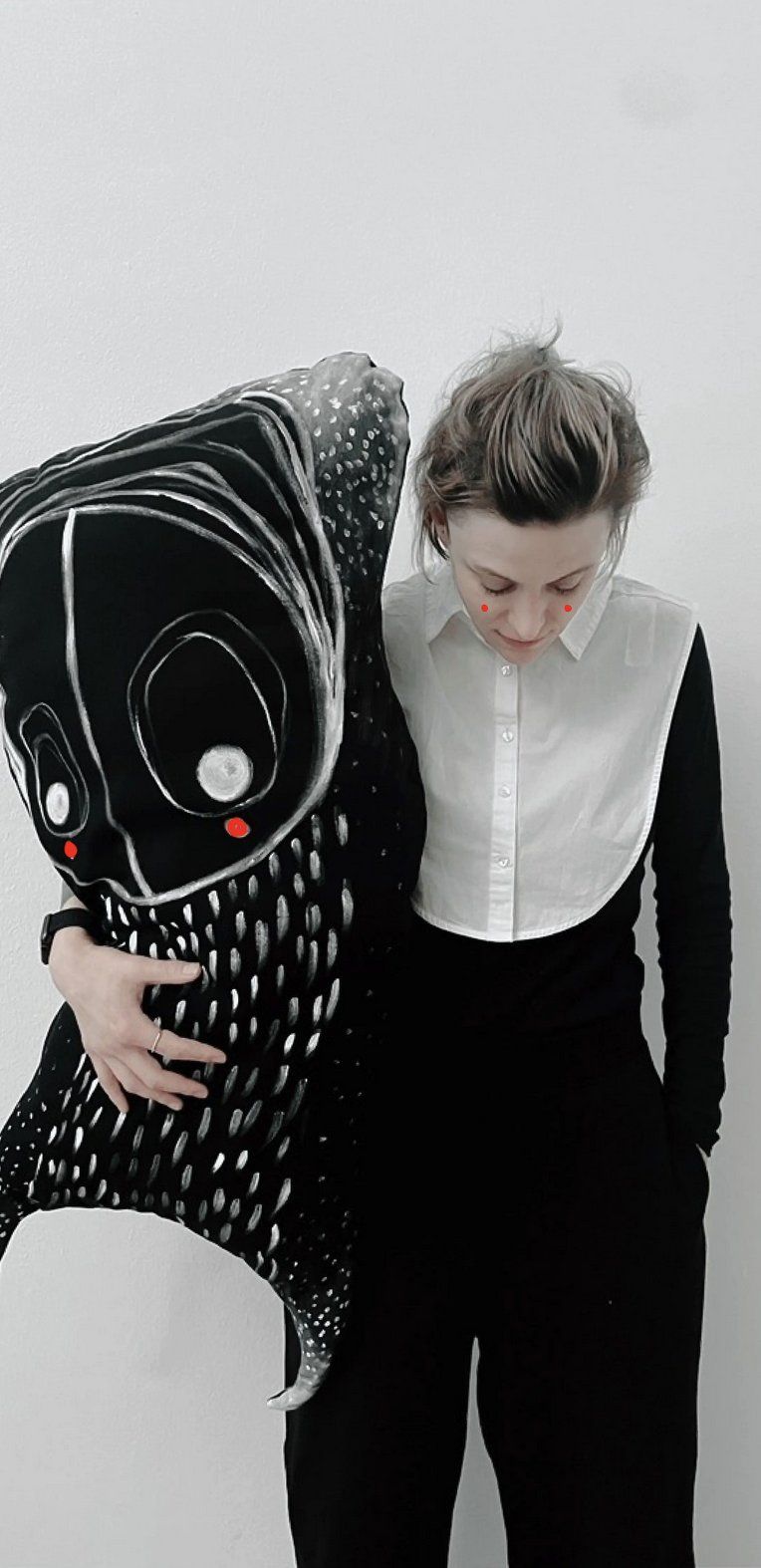 Claudia Six holding a large black-and-white soft sculpture with a drawn face — a quiet moment of connection