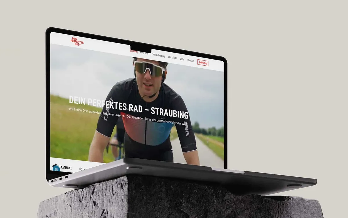 Website: Laptop auf einem Findling im Freien zeigt die Startseite von Dein Perfektes Rad in Straubing mit einem Rennradfahrer im Hero