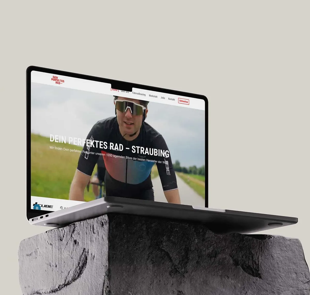Dein perfektes Rad: Laptop auf einem Findling im Freien zeigt die Startseite von Dein Perfektes Rad in Straubing mit einem Rennradfahrer im Hero