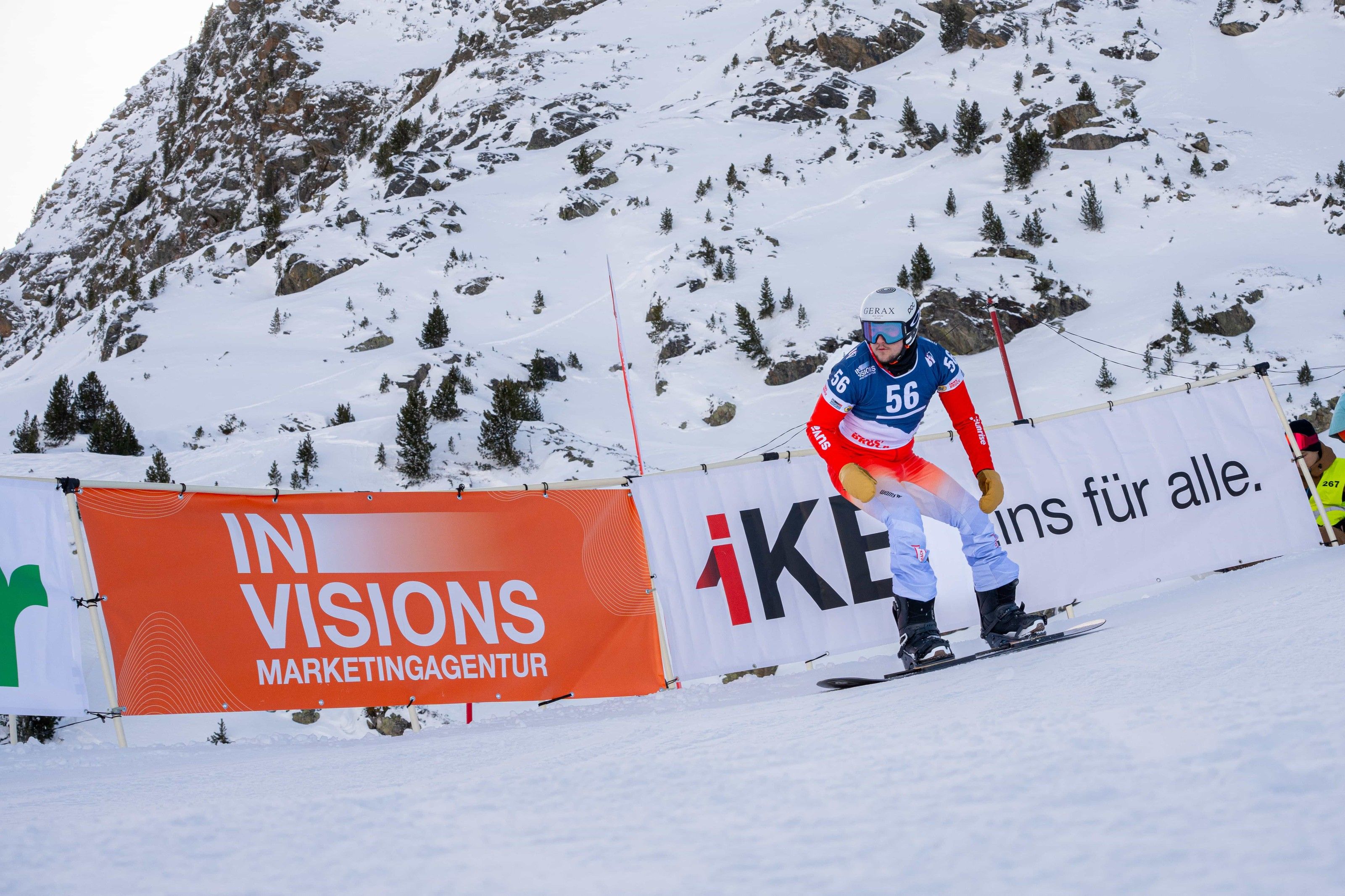 Crazy Curves / FIS Para Snowboard Worldcup: Para-Snowboarder mit Startnummer 56 auf der Rennpiste, davor die orange Bande der Marketingagentur Invisions