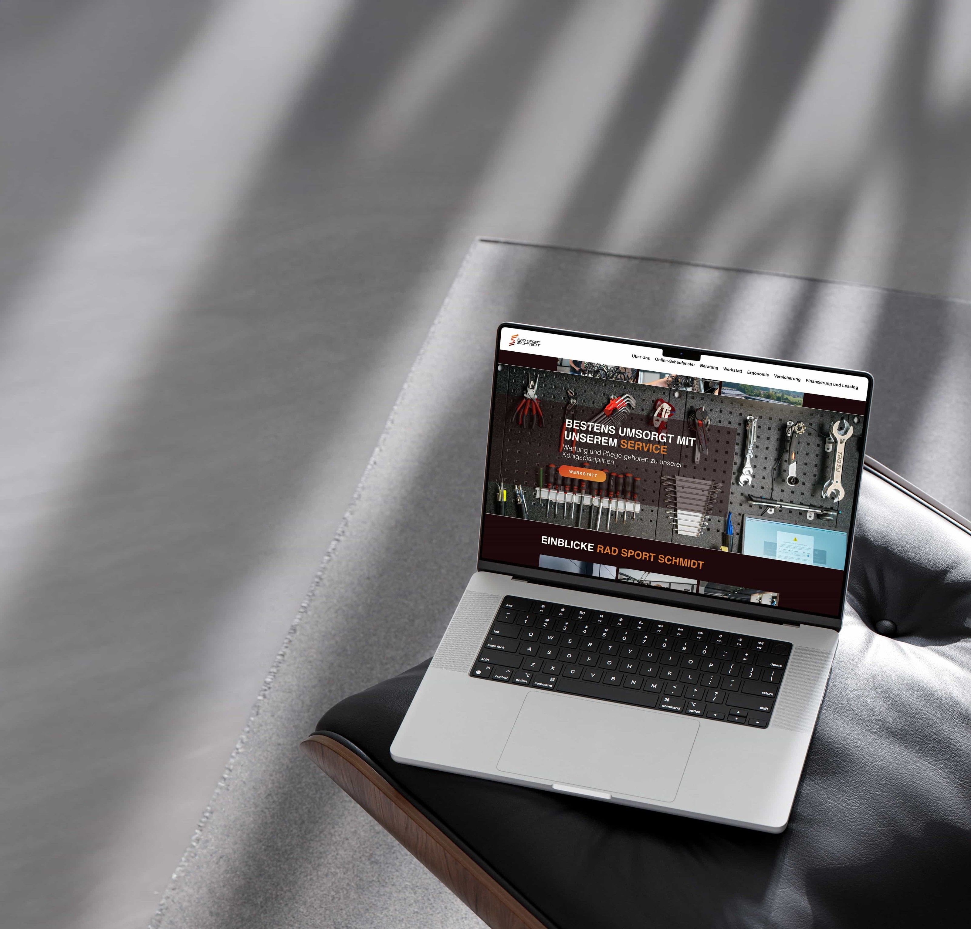 Rad Sport Schmidt: Aufgeklapptes MacBook im Streiflicht zeigt eine dunkel gestaltete Website mit Werkzeug- und Produktabbildungen