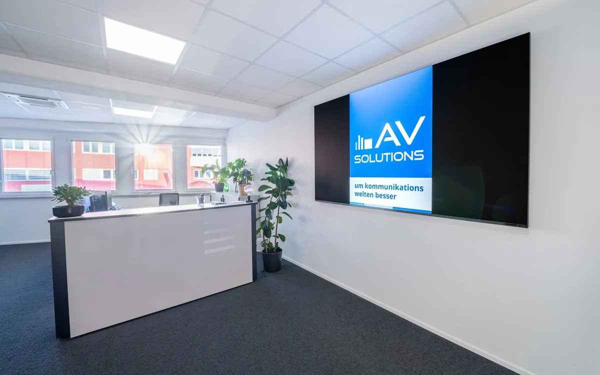 Personalfotografie: Empfangsbereich eines Büros mit langer Bildschirmwand, auf der das Logo von AV Solutions läuft