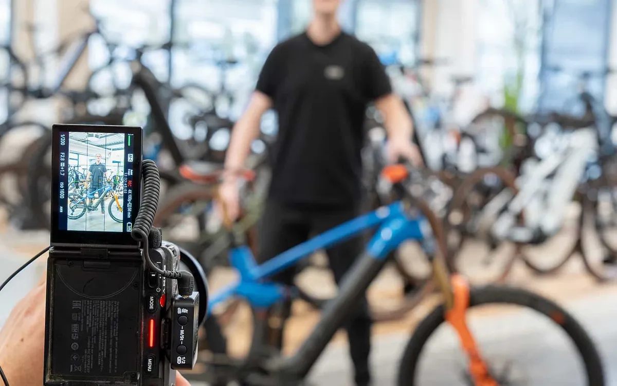 Fachhandelspartner: Blick über das Display einer Filmkamera auf einen Mitarbeiter, der ein Mountainbike durch den Verkaufsraum schiebt