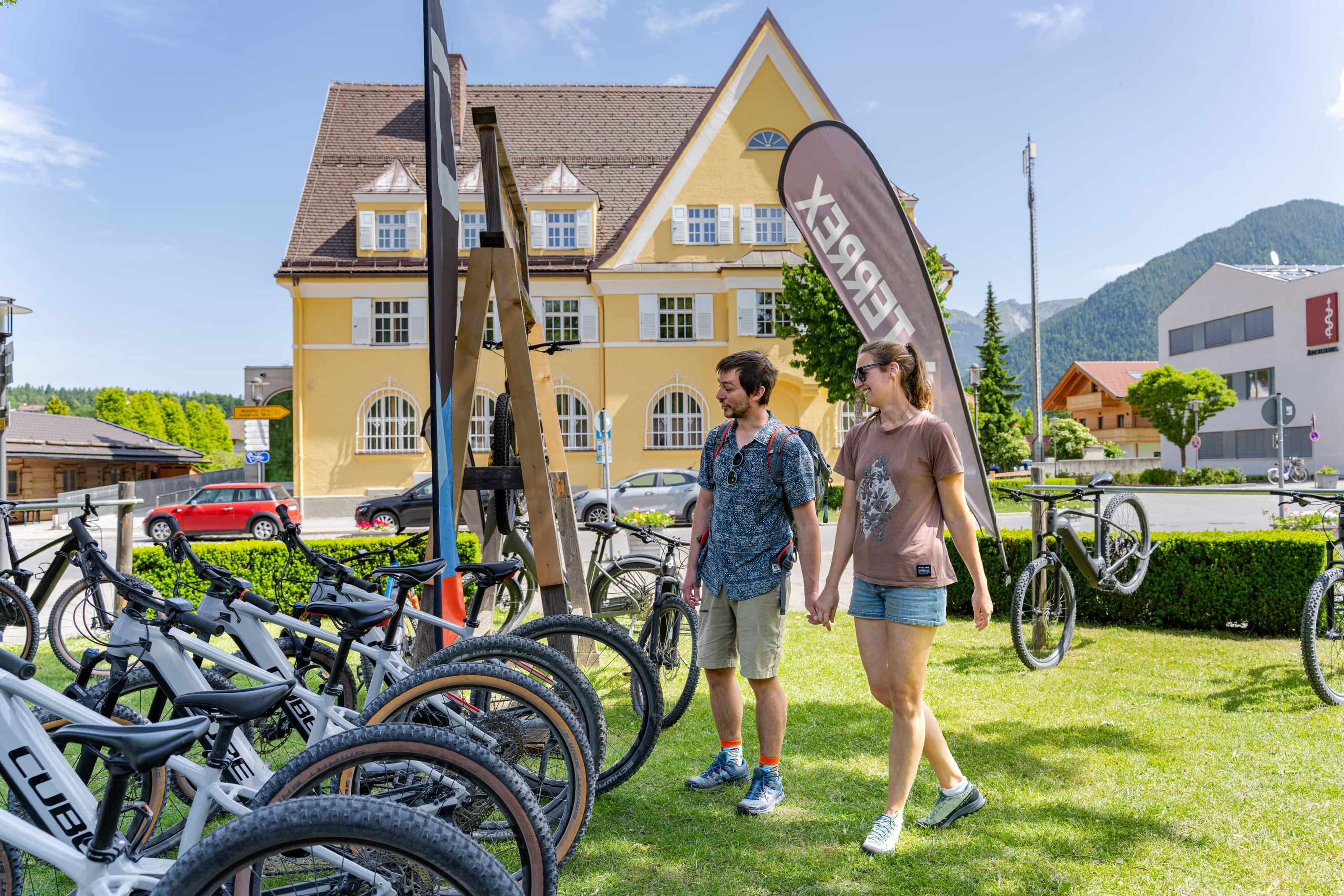 Sports Max Rieger: Reihe von CUBE-Bikes vor einem gelben Gasthaus, ein Paar geht am Verleih vorbei