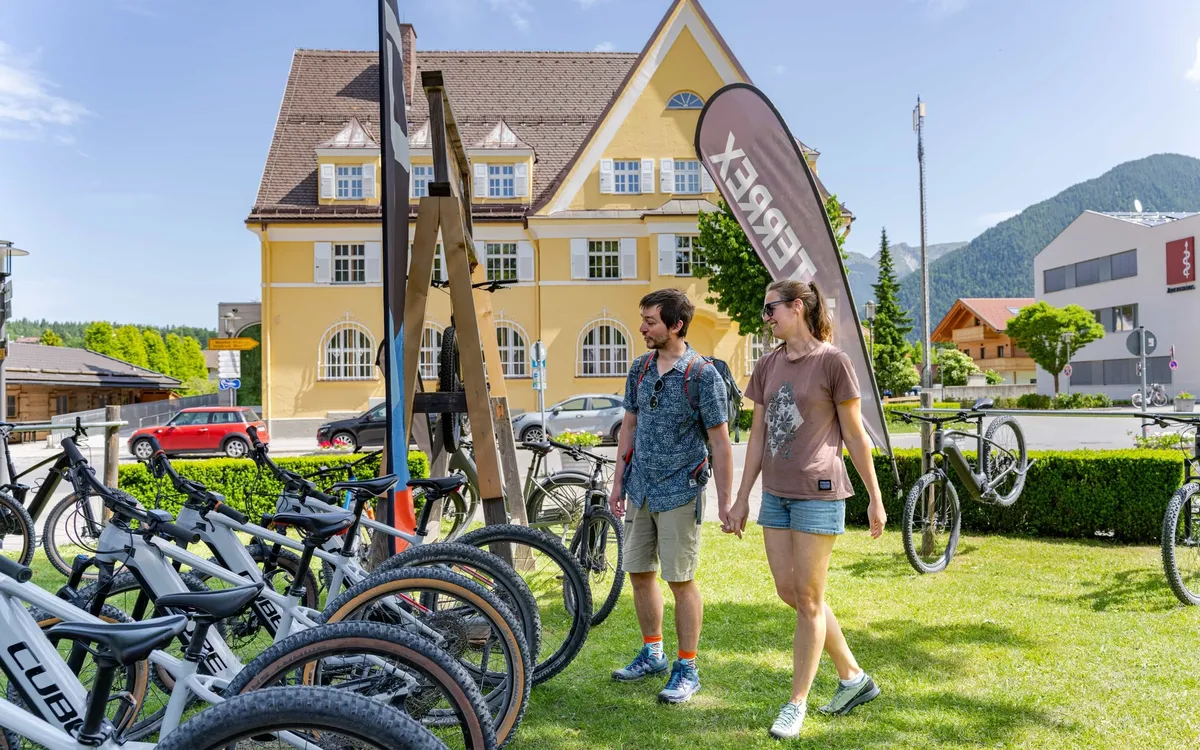 Sports Max Rieger: Reihe von CUBE-Bikes vor einem gelben Gasthaus, ein Paar geht am Verleih vorbei