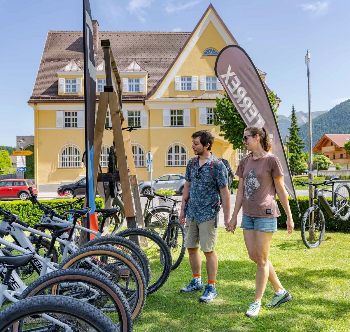 Sports Max Rieger: Reihe von CUBE-Bikes vor einem gelben Gasthaus, ein Paar geht am Verleih vorbei