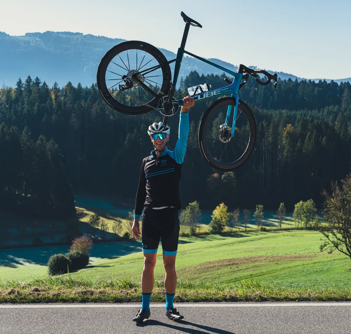 CUBE Store Valbirse: Ein Fahrer hebt sein Rennrad über den Kopf, hinter ihm der bewaldete Jura.