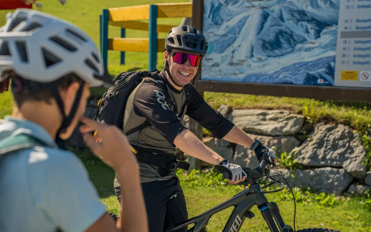 Imagefilm und Videocontent: Zwei Mountainbiker mit Helmen im Gespräch vor einer Panoramatafel