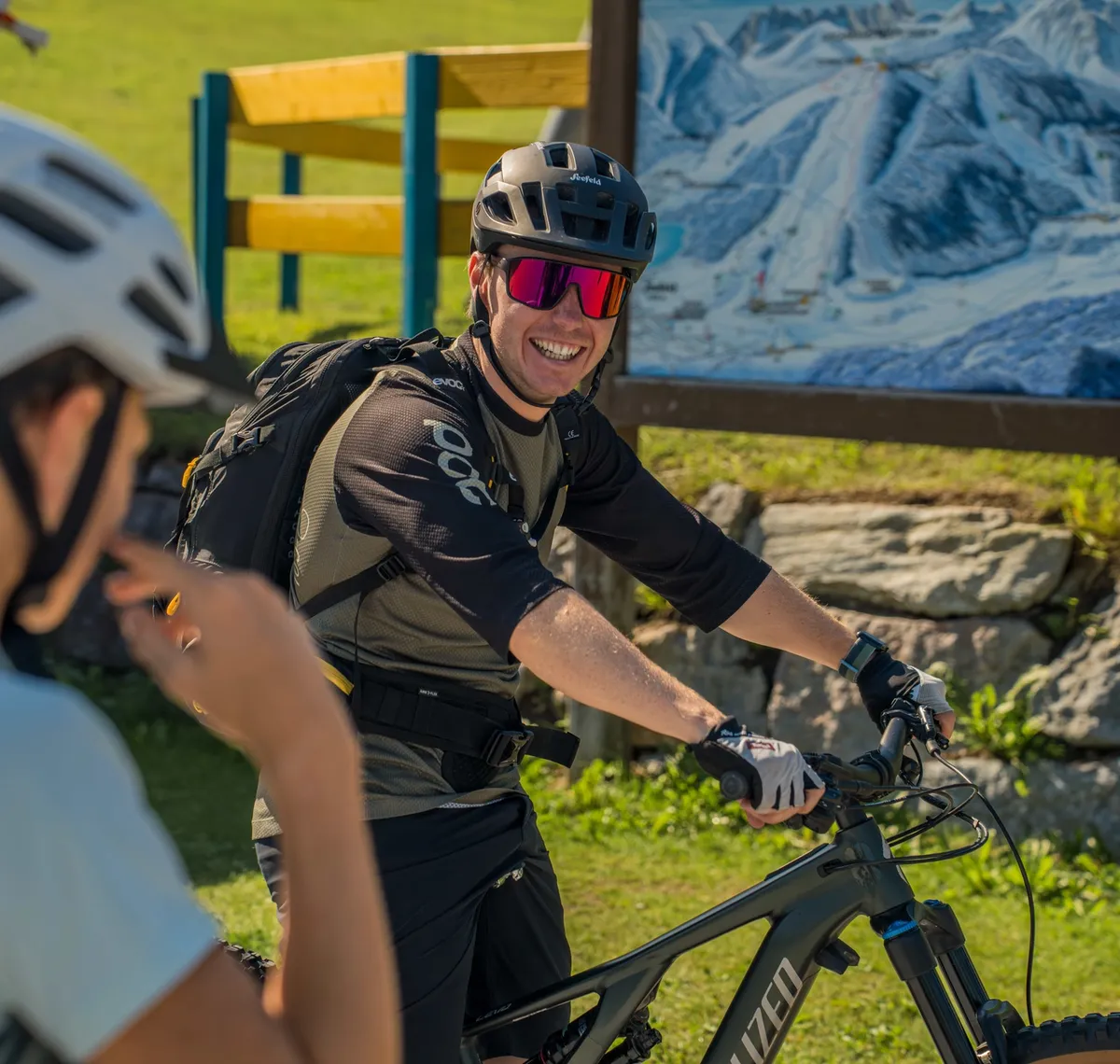 Bike & Hike: Zwei Mountainbiker mit Helmen im Gespräch vor einer Panoramatafel