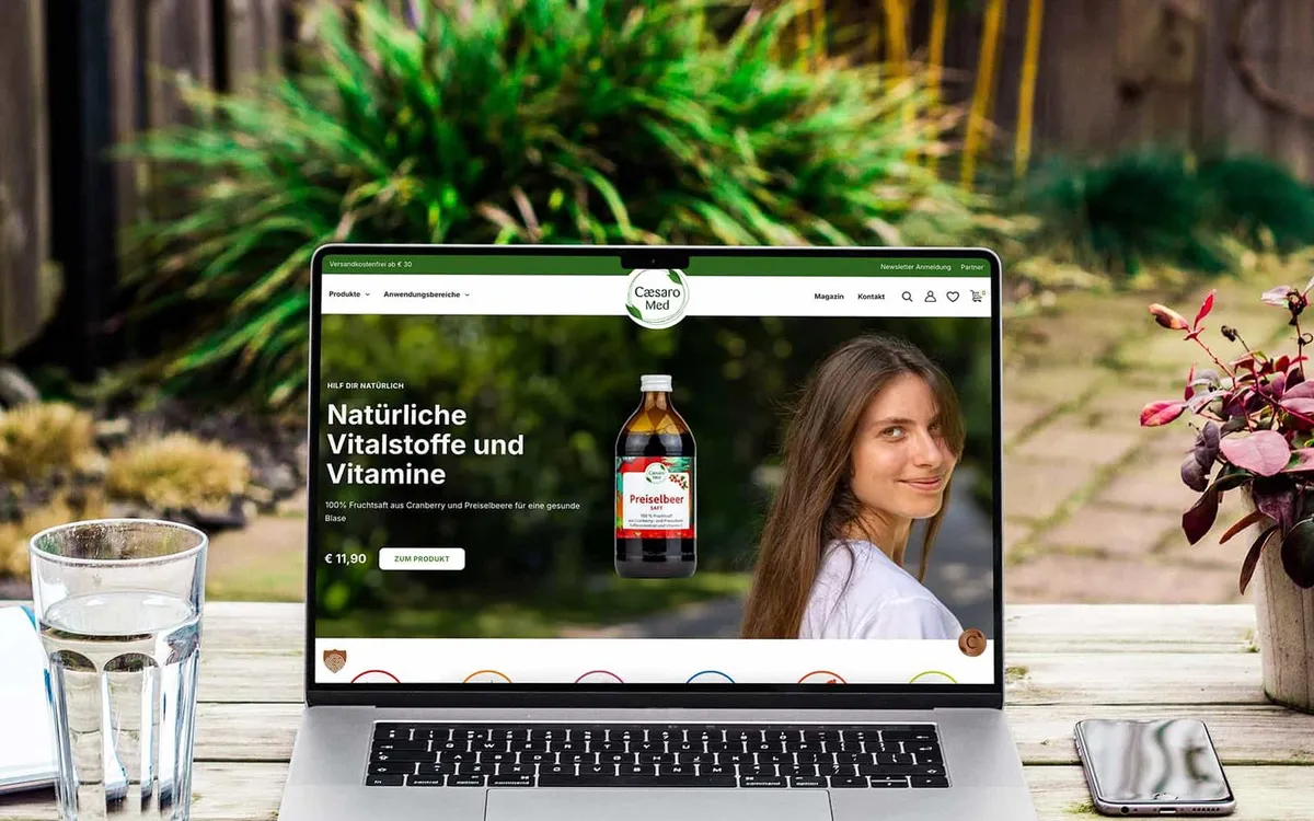 Webdesign: Laptop auf einem Gartentisch zeigt den Caesaro-Med-Shop mit der Zeile „Natürliche Vitalstoffe und Vitamine"