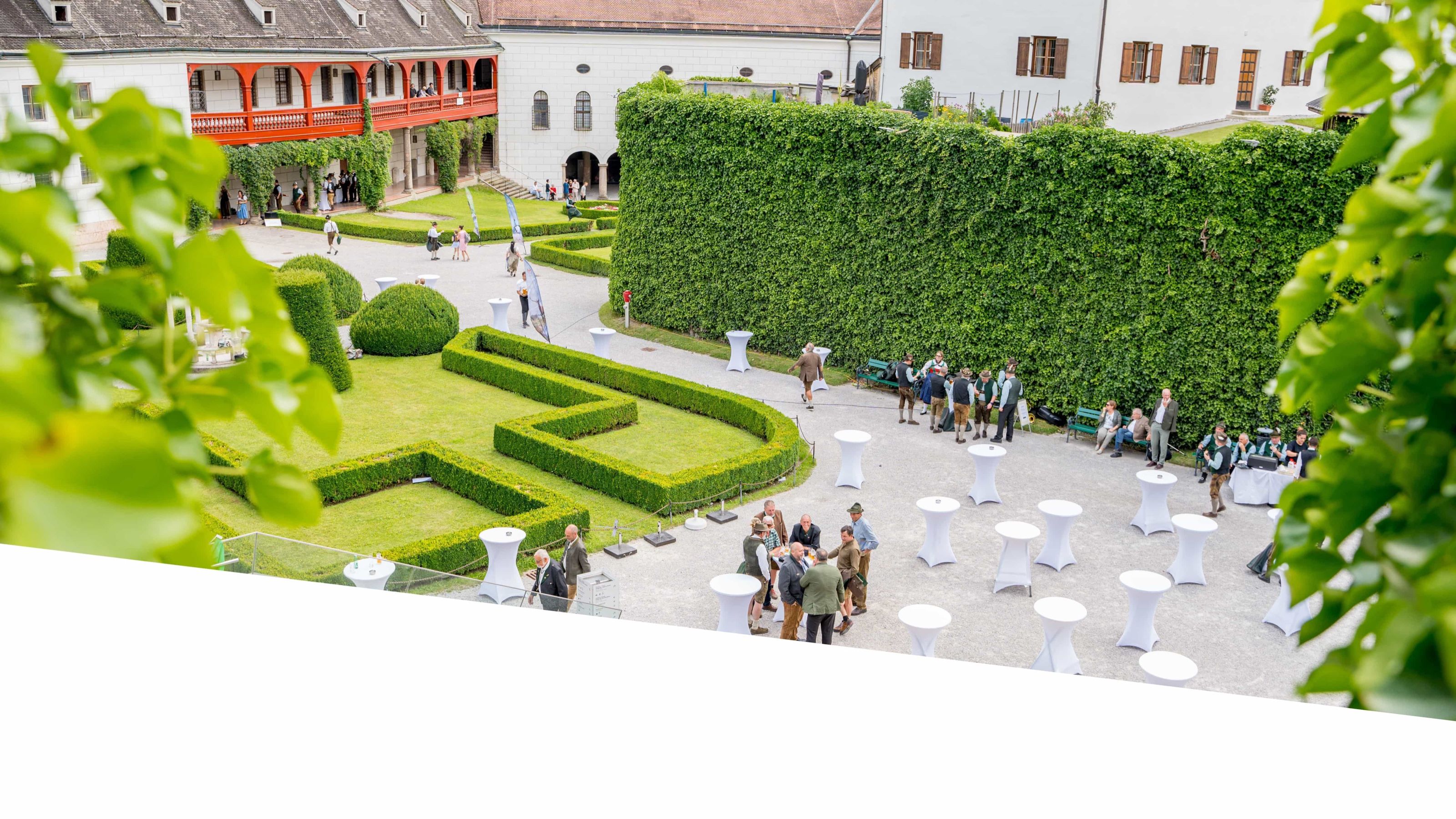 Inntal Catering: Blick von oben auf einen Barockgarten mit Hecken, Stehtischen und Gästen