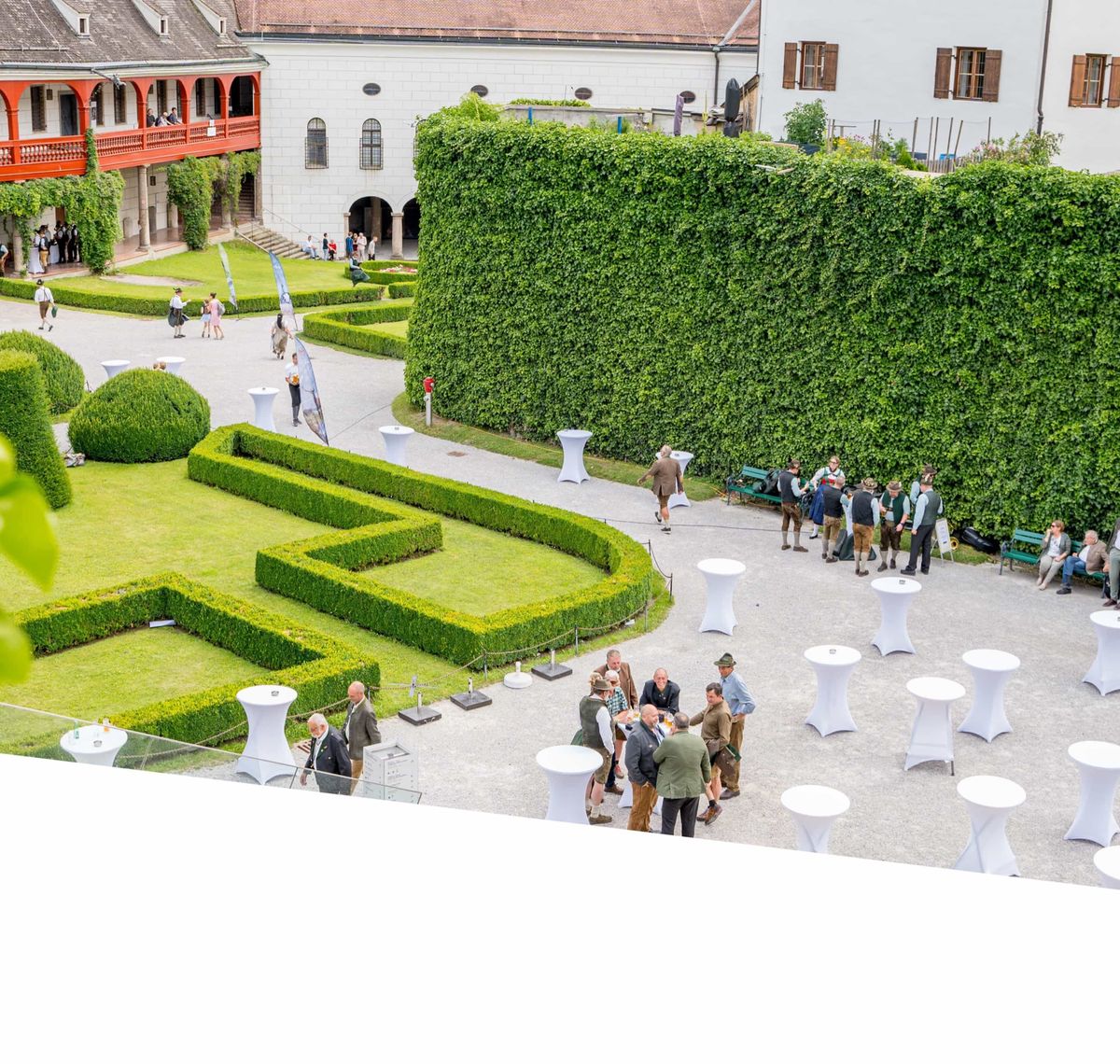 Inntal Catering: Blick von oben auf einen Barockgarten mit Hecken, Stehtischen und Gästen