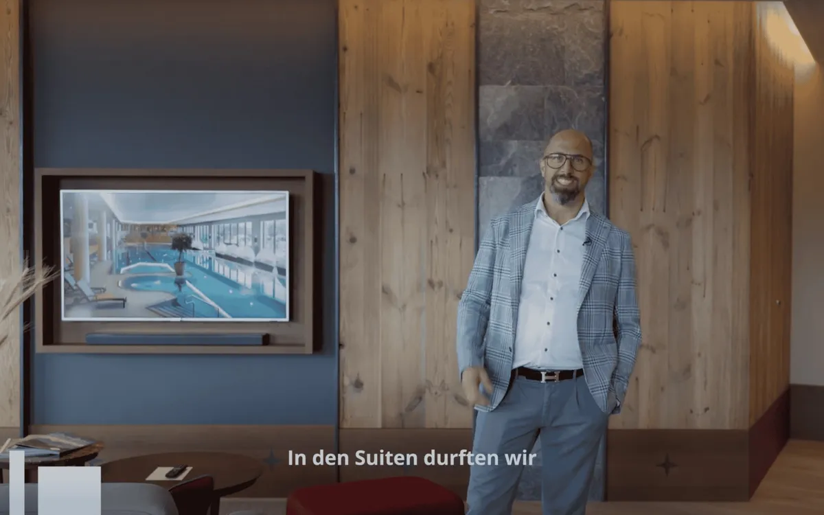 Videoproduktion: Filmstill aus einem Imagefilm: ein Mann im Sakko steht in einem holzvertäfelten Hotelflur