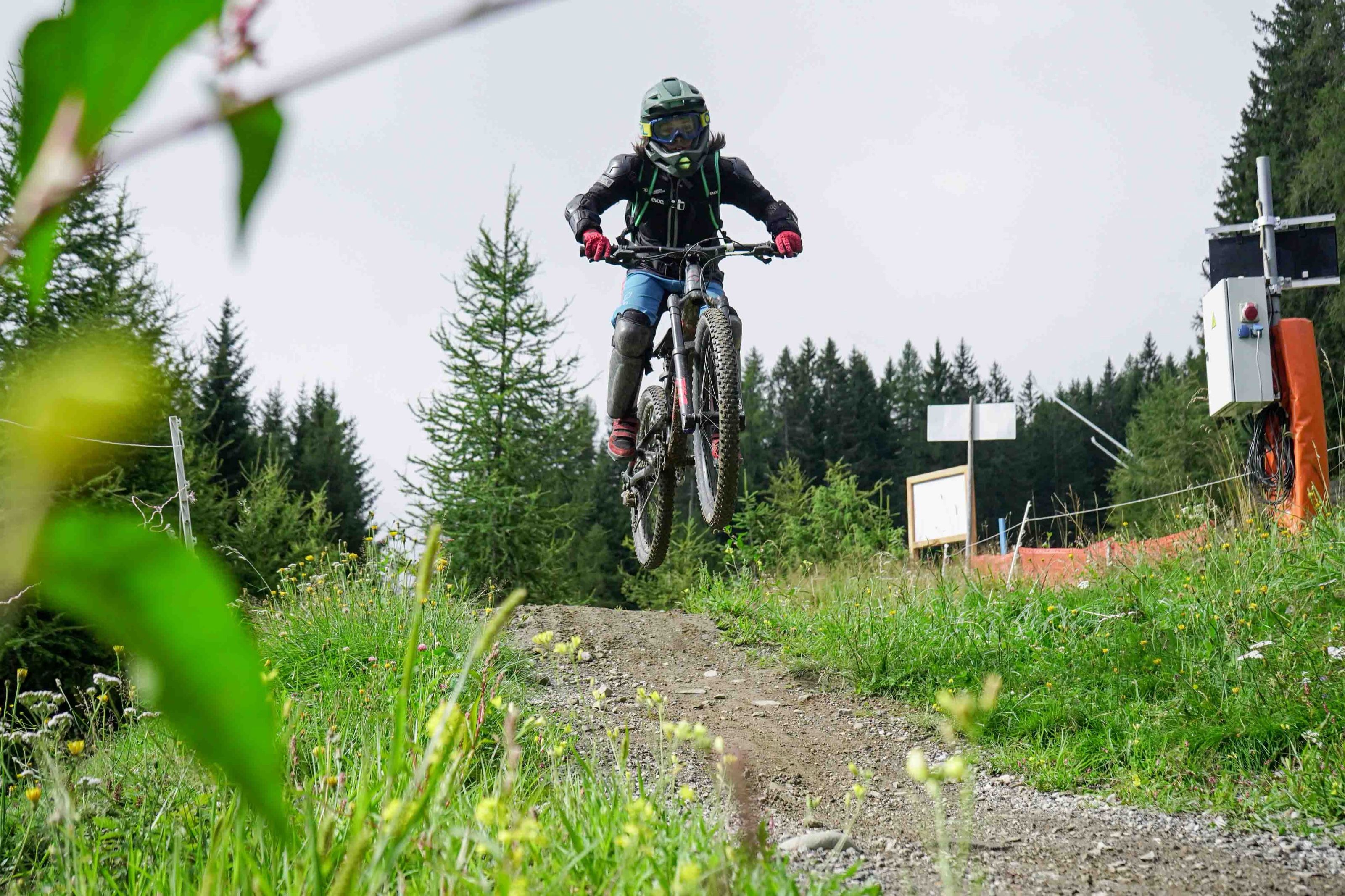 MTB & Downhill Verein Tirol: Downhill-Fahrer springt über eine Kuppe der Bikepark-Strecke, dahinter Nadelwald
