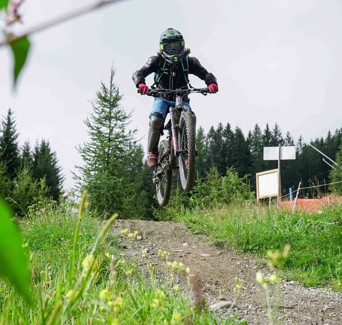 MTB & Downhill Verein Tirol: Downhill-Fahrer springt über eine Kuppe der Bikepark-Strecke, dahinter Nadelwald