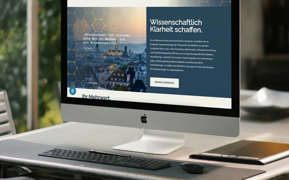 Website: iMac auf einem Schreibtisch zeigt die ActuQuant-Startseite mit der Zeile „Wissenschaftlich Klarheit schaffen"