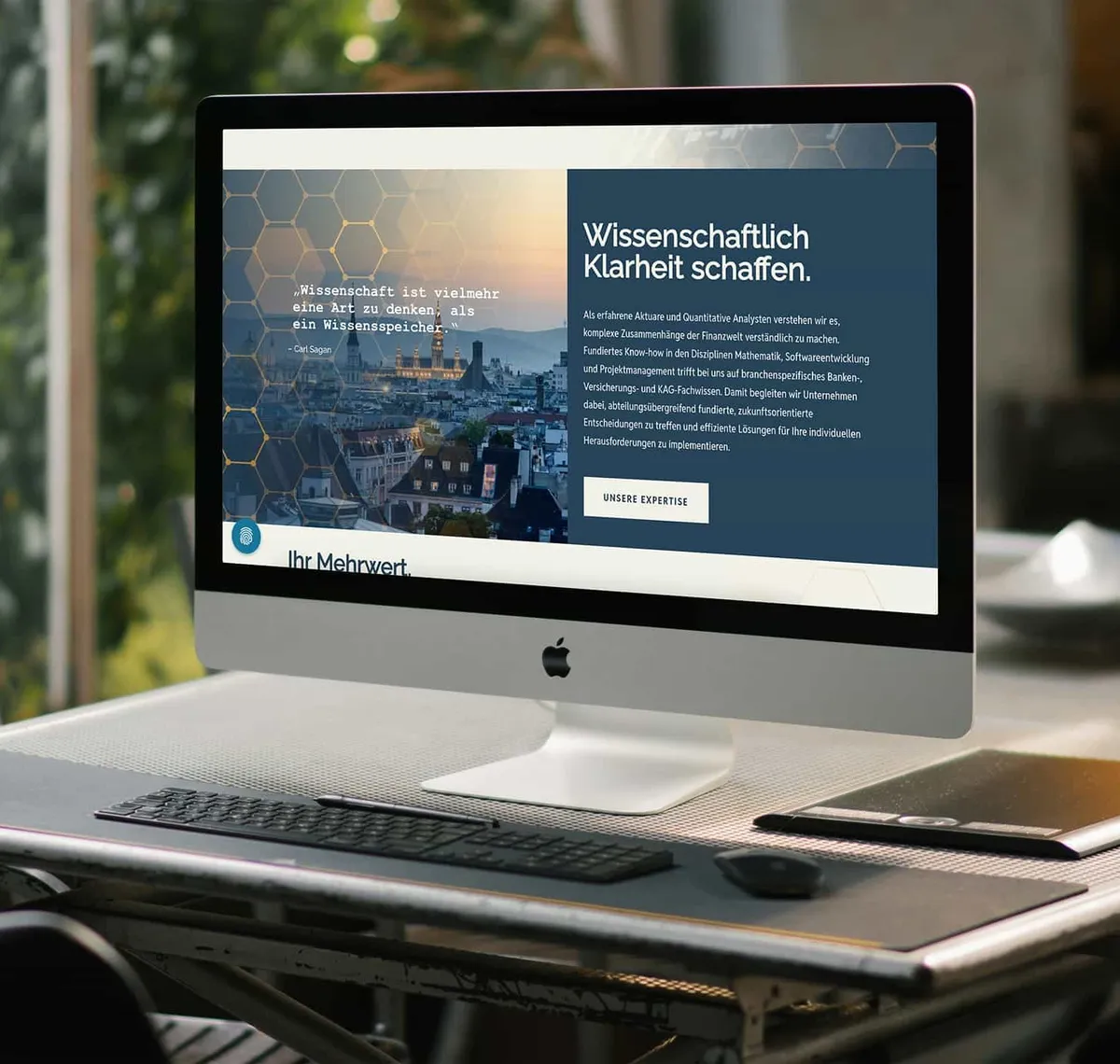 ActuQuant: iMac auf einem Schreibtisch zeigt die ActuQuant-Startseite mit der Zeile „Wissenschaftlich Klarheit schaffen"