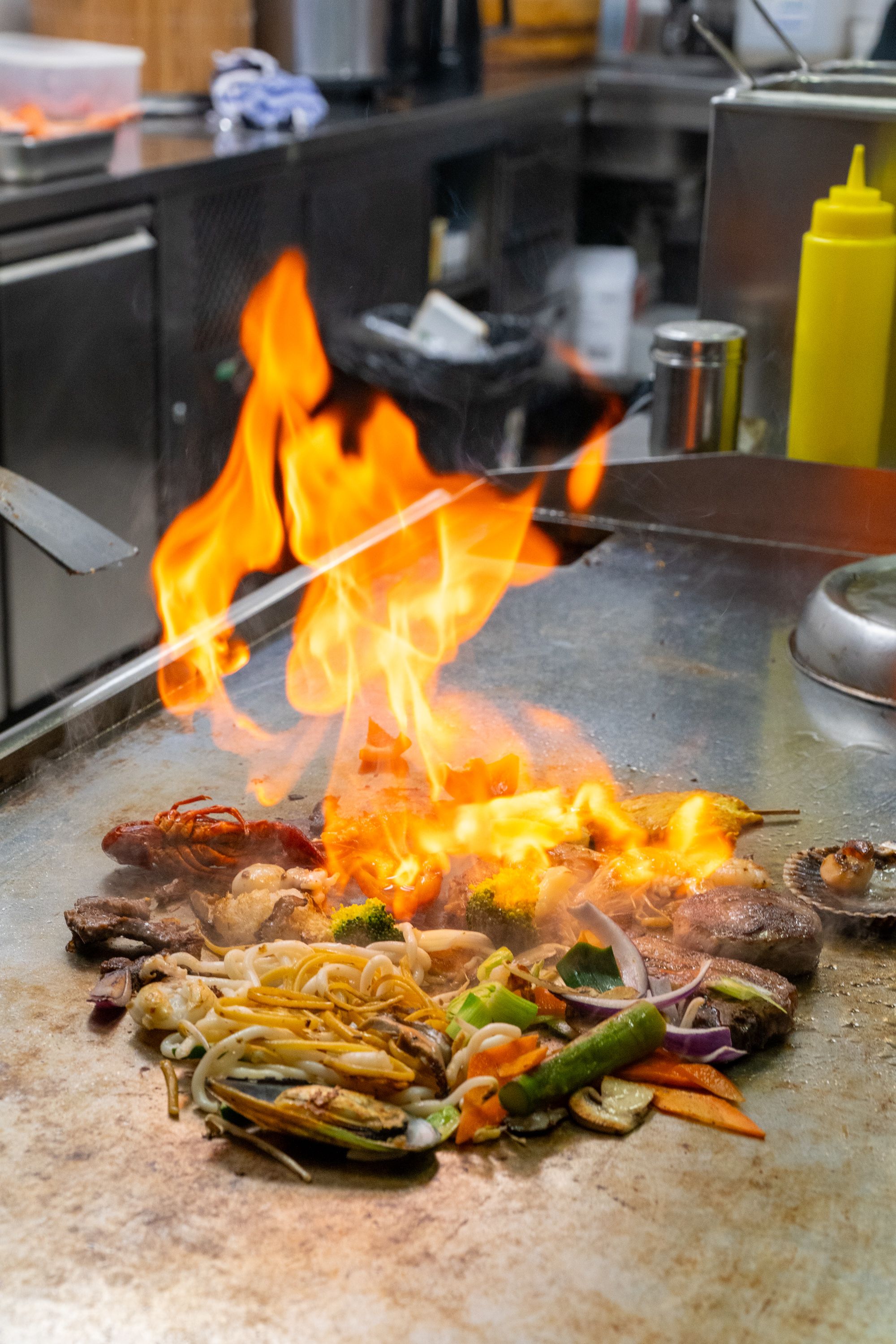Asia Restaurant YAMI: Eine hohe Flamme über der Teppanyaki-Platte, davor Gemüse und Meeresfrüchte auf der heissen Fläche.