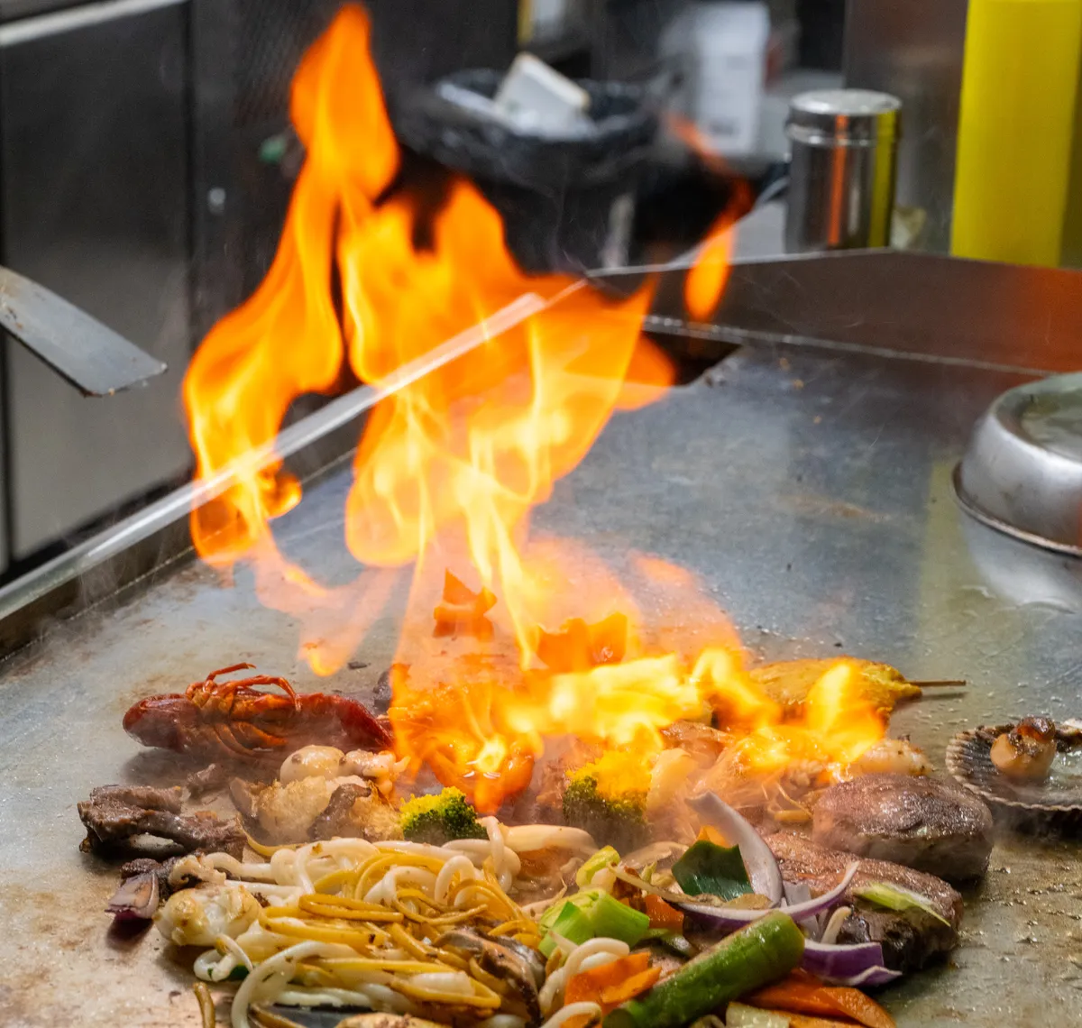 Asia Restaurant YAMI: Eine hohe Flamme über der Teppanyaki-Platte, davor Gemüse und Meeresfrüchte auf der heissen Fläche.