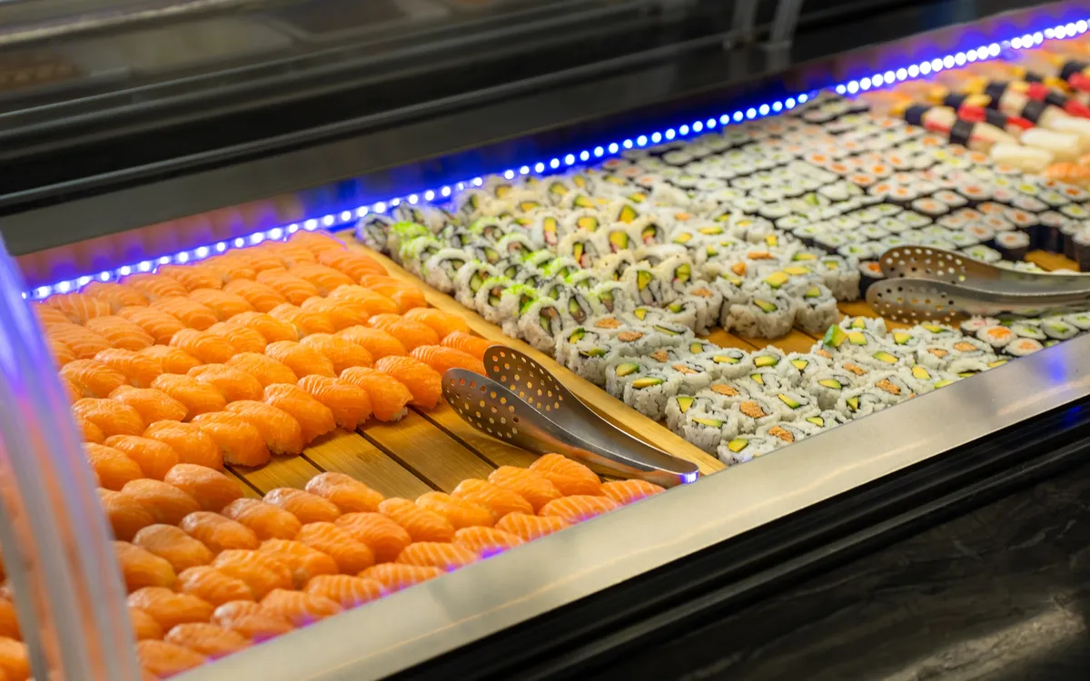 TikTok für ein Asia-Restaurant: Reihen Lachs-Nigiri und Maki-Rollen in der Buffetvitrine, darüber das blaue Lichtband der Sushitheke.