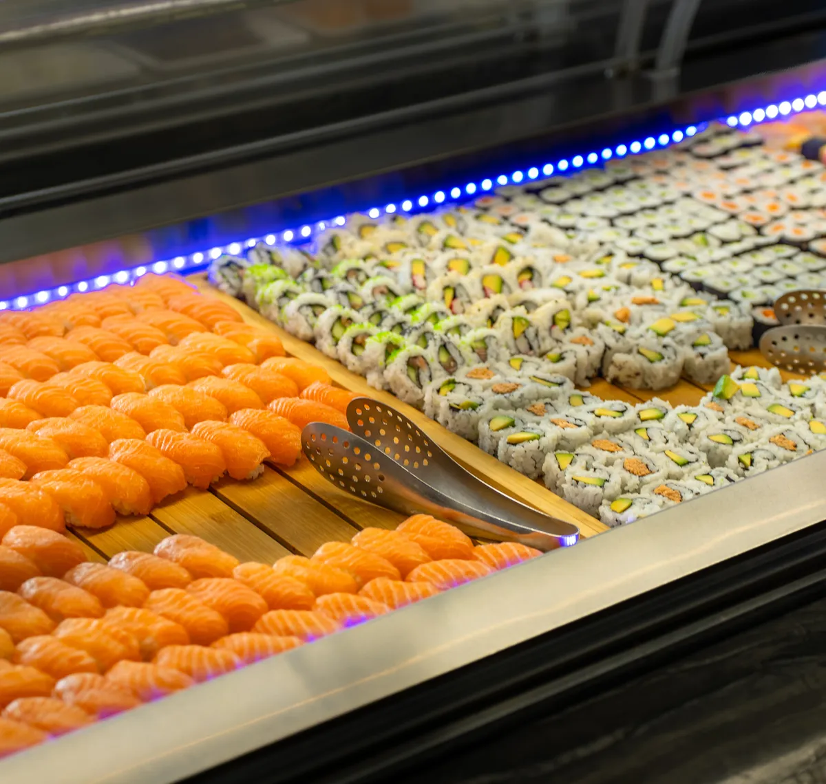 Asia Restaurant YAMI: Reihen Lachs-Nigiri und Maki-Rollen in der Buffetvitrine, darüber das blaue Lichtband der Sushitheke.