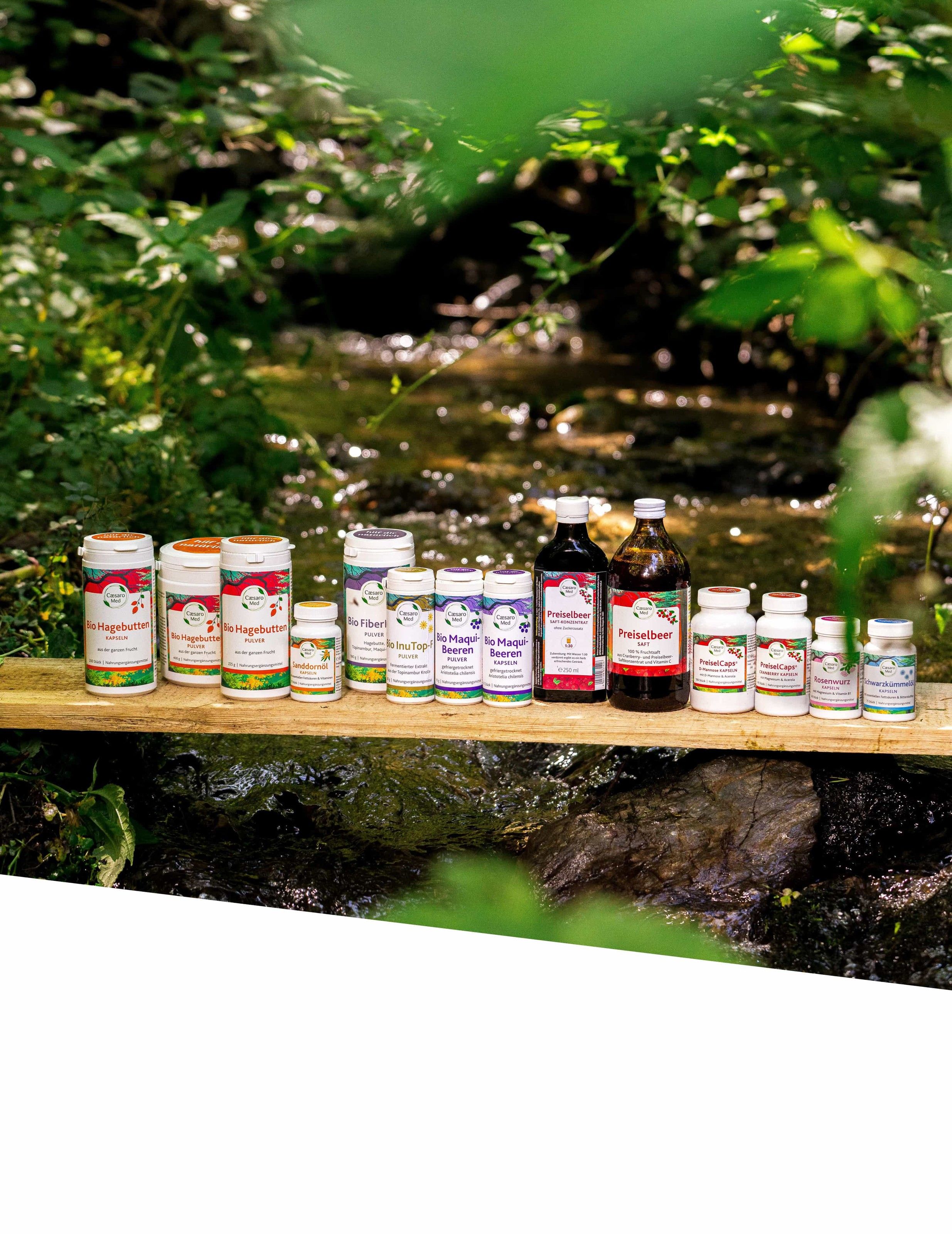APOfit: Produktflaschen einer Naturprodukt-Serie auf einem Holzbrett vor einer bemoosten Quelle