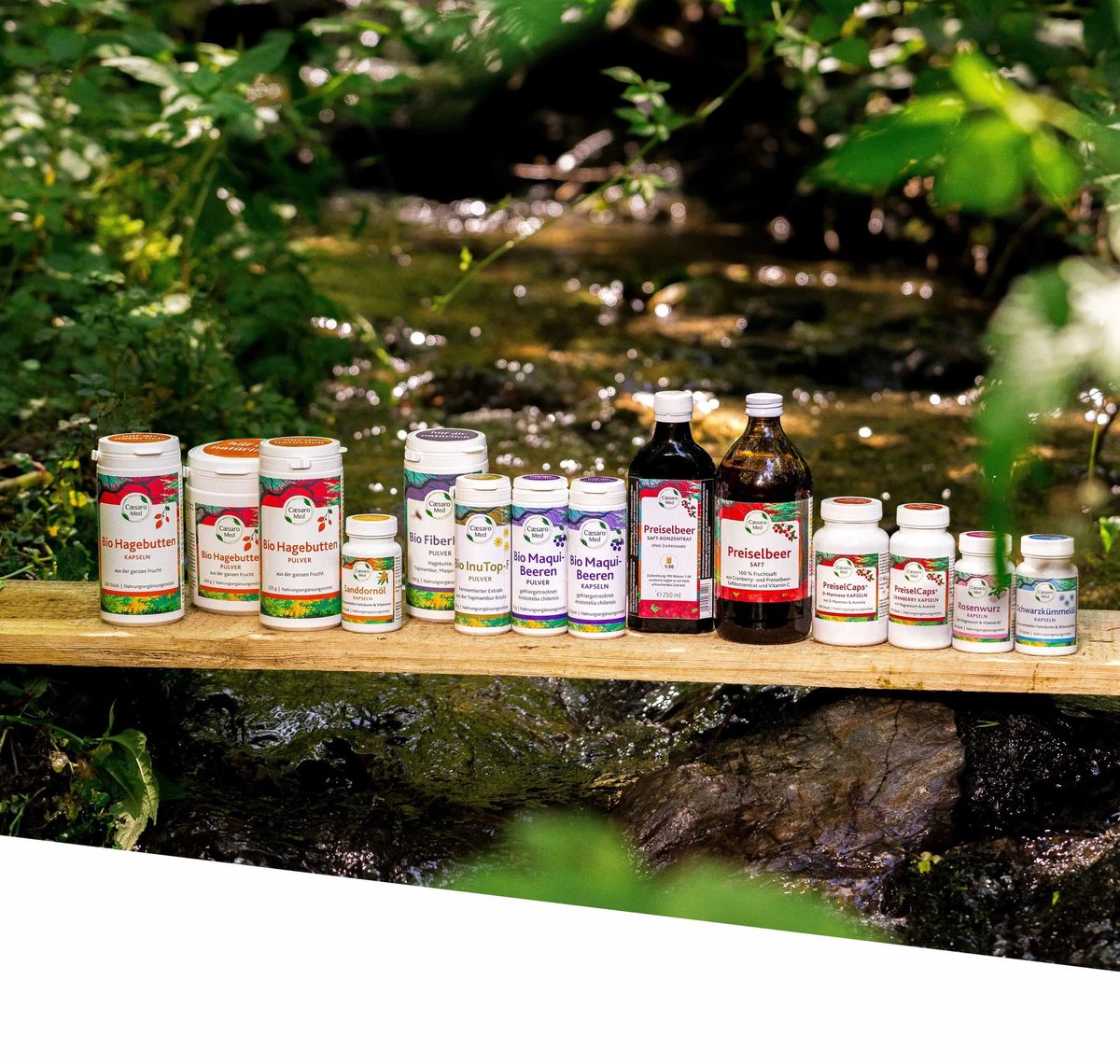 APOfit: Produktflaschen einer Naturprodukt-Serie auf einem Holzbrett vor einer bemoosten Quelle