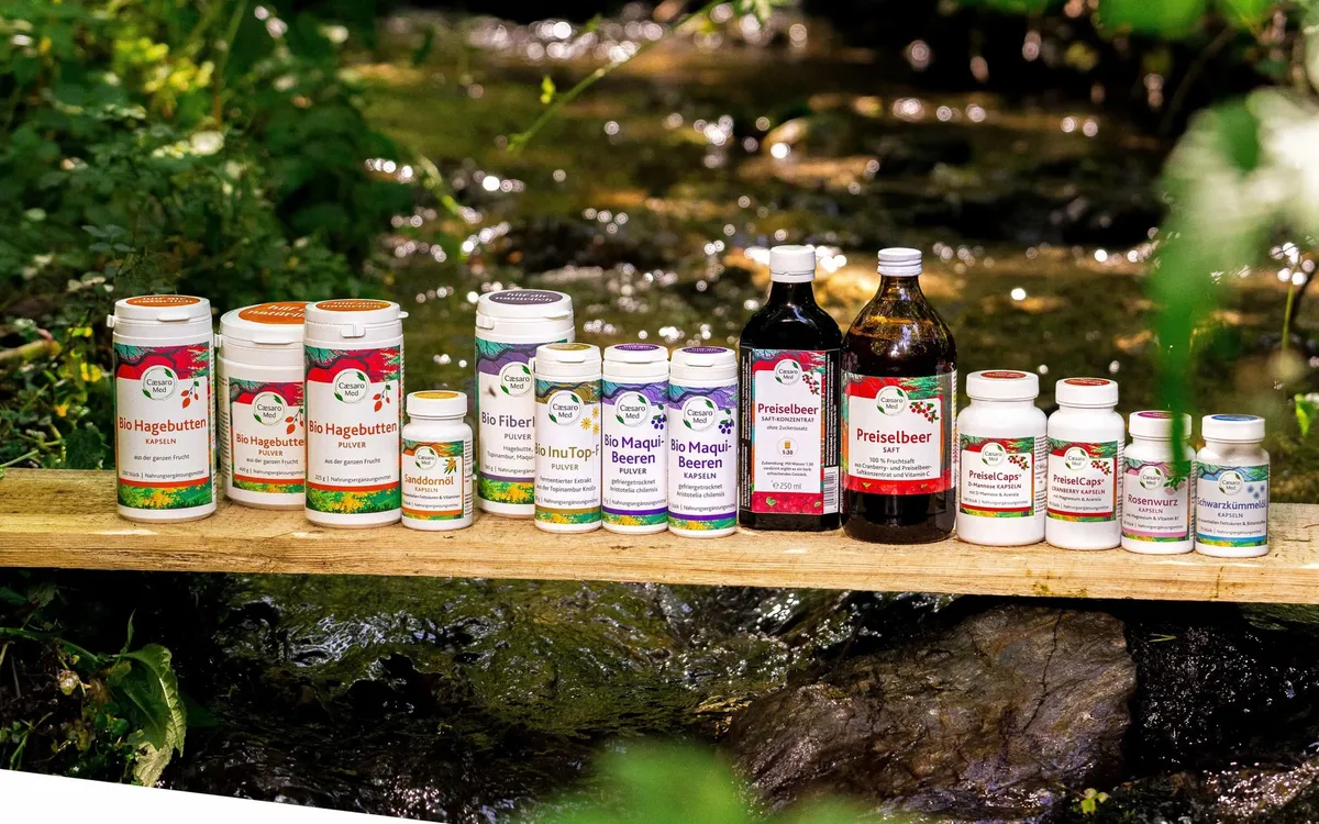 APOfit: Produktflaschen einer Naturprodukt-Serie auf einem Holzbrett vor einer bemoosten Quelle