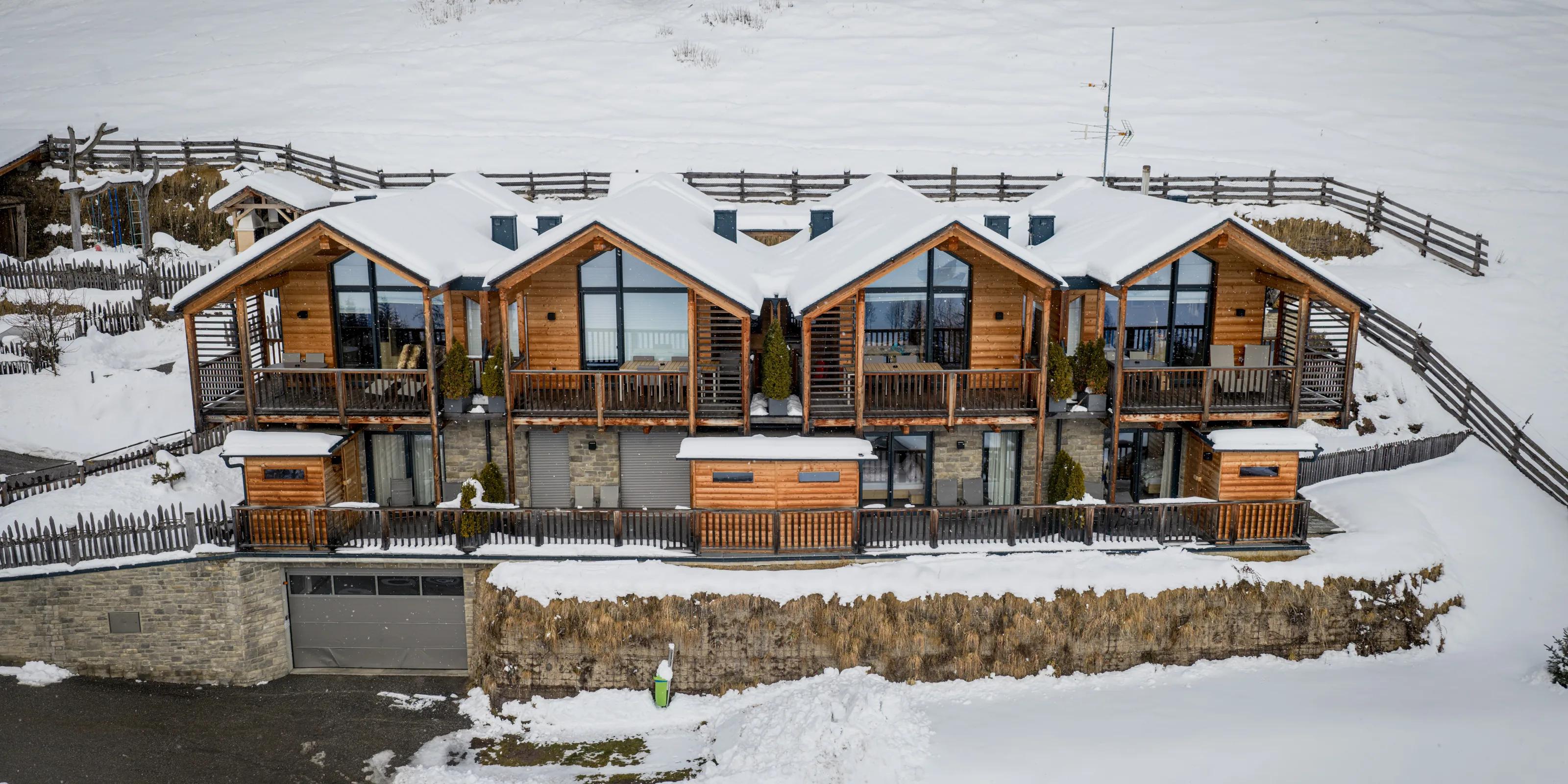 Stabinger Hof: Die vier Chalets des Stabinger Hof im Winter aus der Luft, Holzfassaden und verglaste Giebel hinter verschneiten Wiesen.
