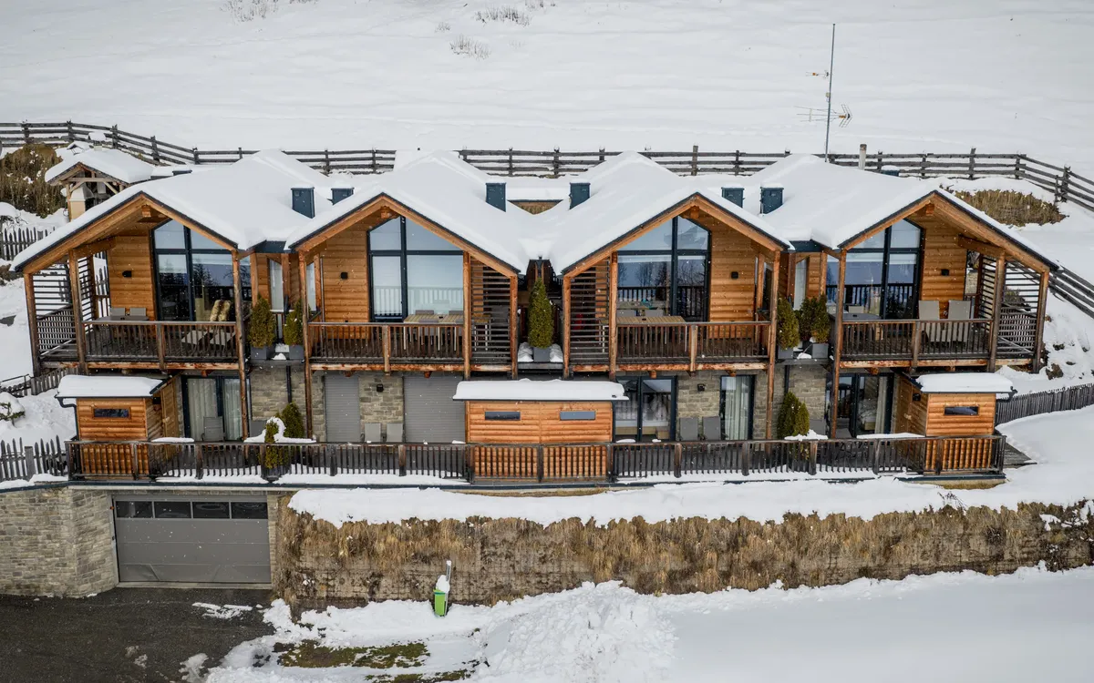 Stabinger Hof: Die vier Chalets des Stabinger Hof im Winter aus der Luft, Holzfassaden und verglaste Giebel hinter verschneiten Wiesen.