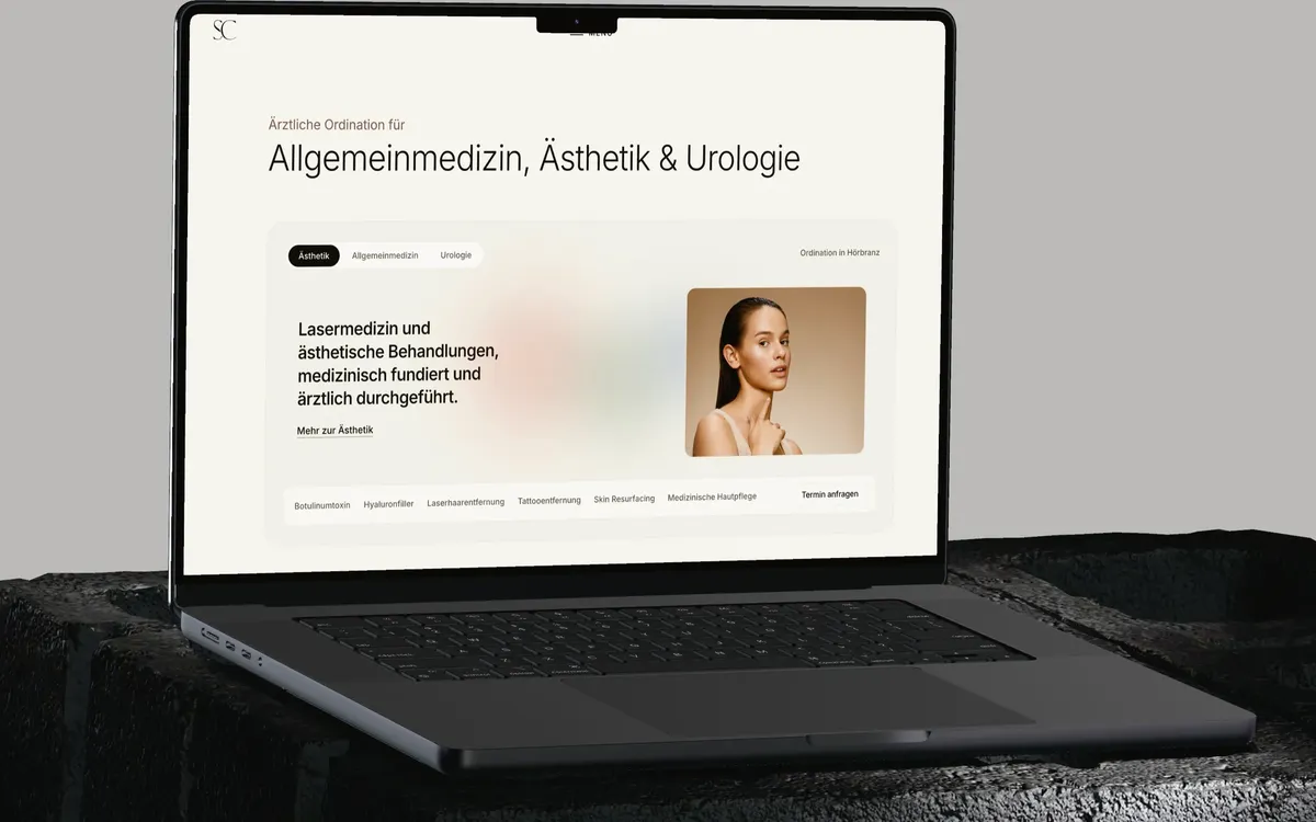 Skinchic.Med: Ein MacBook auf einem dunklen Steinsockel vor hellgrauem Grund zeigt die Startseite von skinchic.at mit den drei Fachbereichen Ästhetik, Allgemeinmedizin und Urologie.