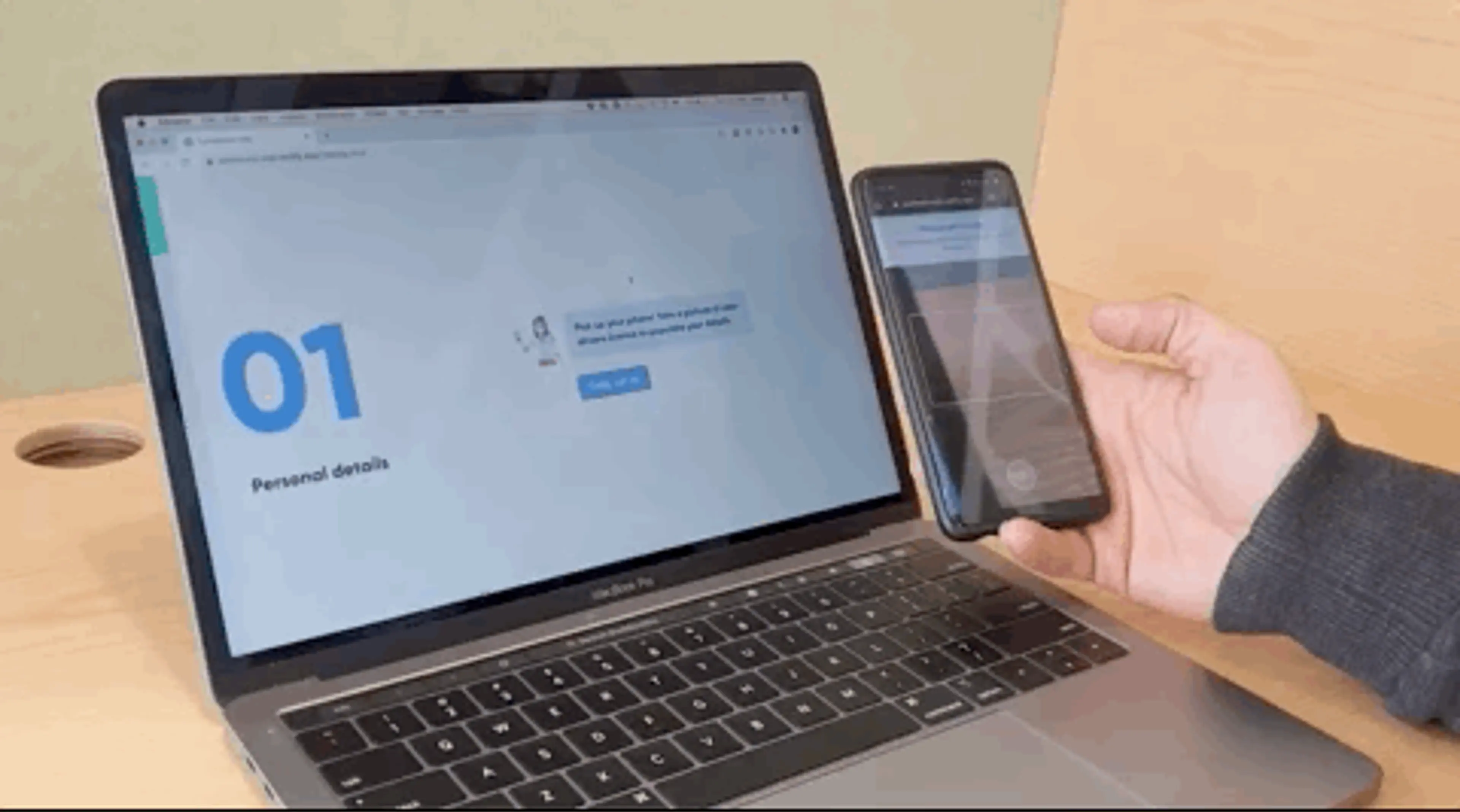 A person holding a mobile phone to a laptop