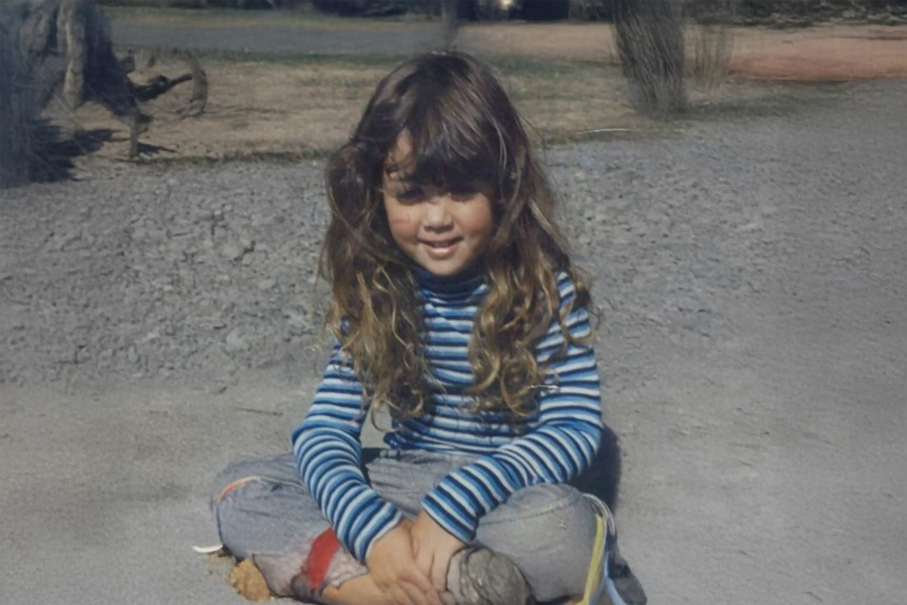 A photo of a little girl sitting crossed-legged on gravel